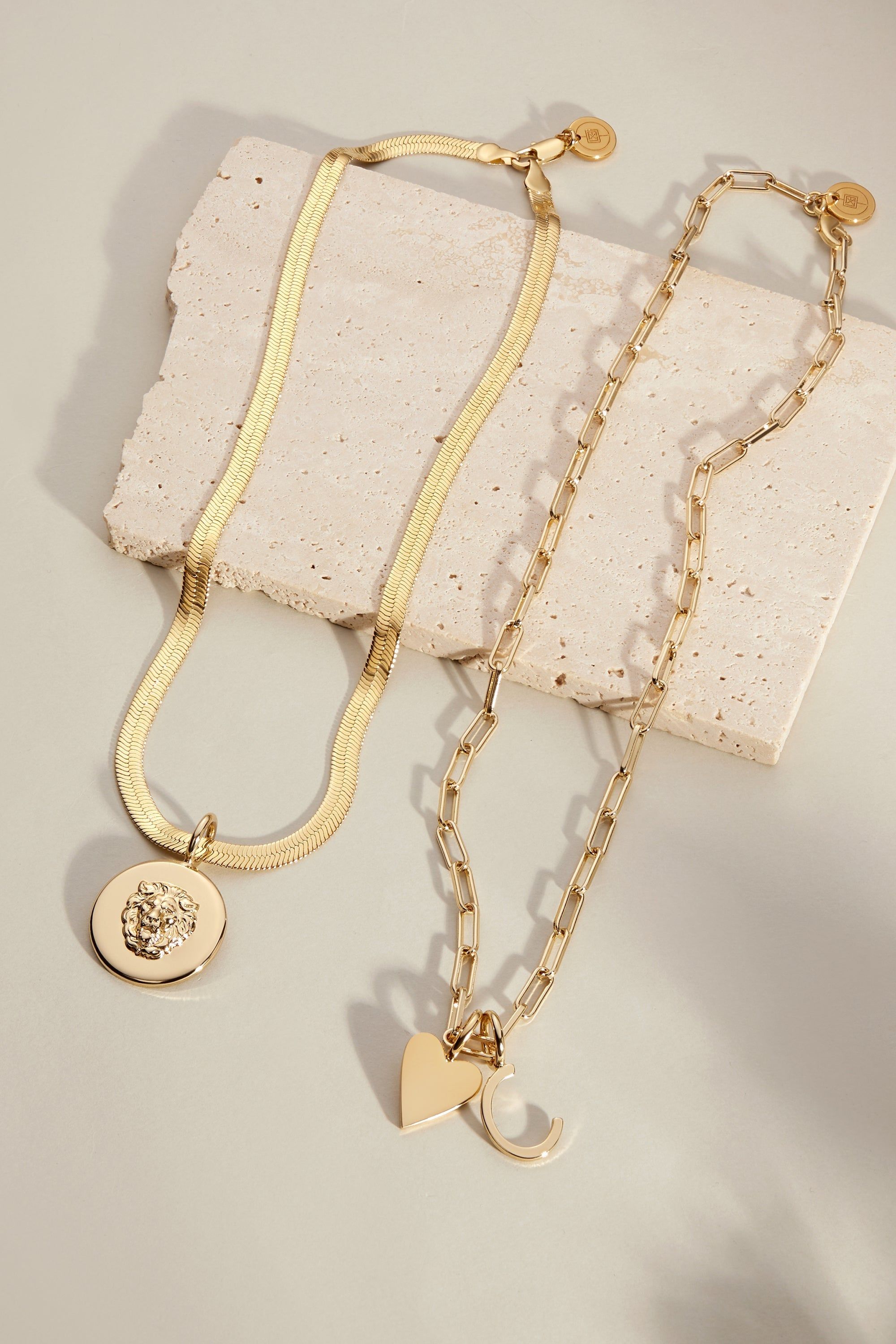 Two gold-toned necklaces from the Cara Charm Necklace collection displayed beautifully