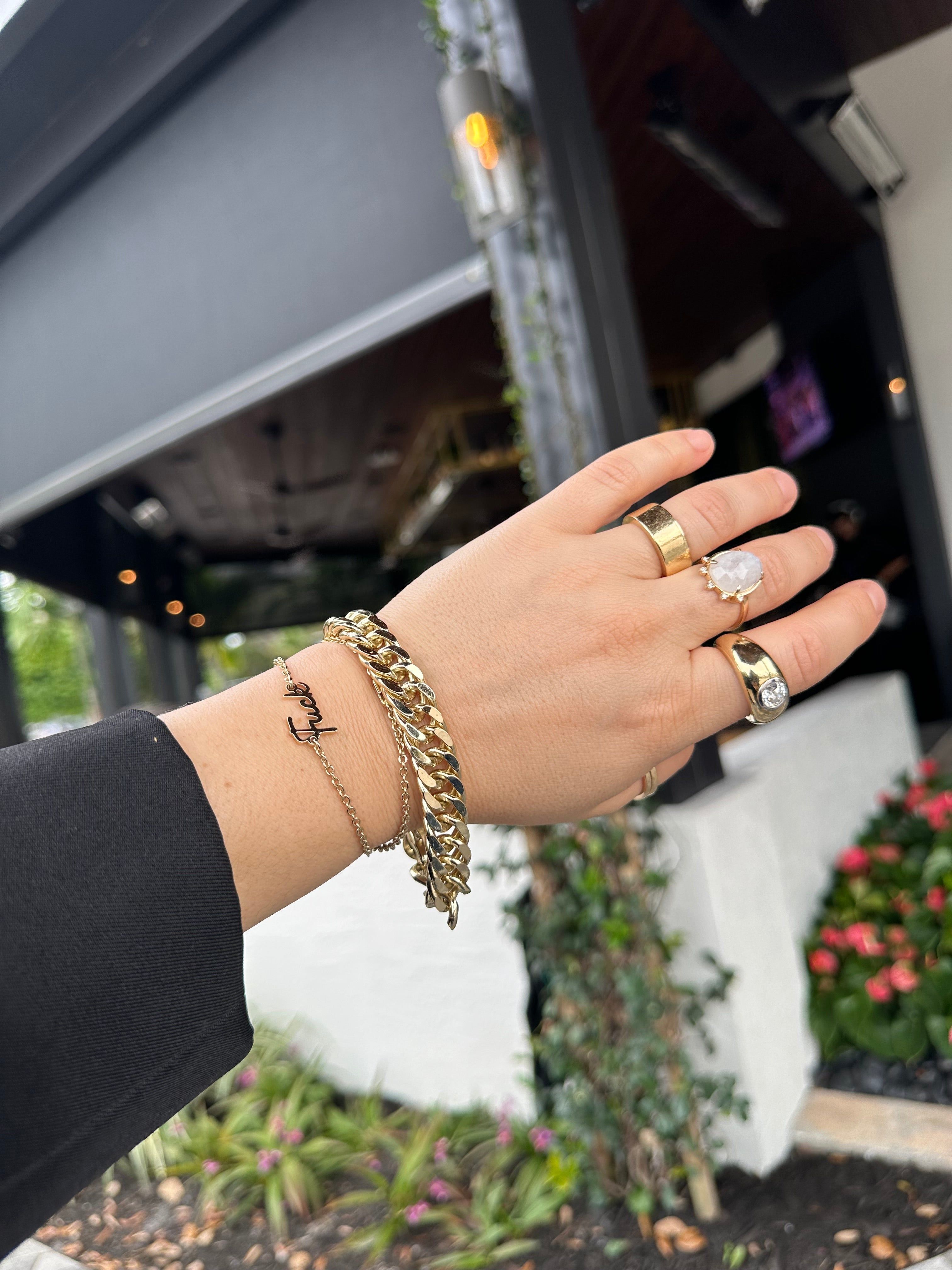 Hand with gold jewelry showcasing the Dainty Script Fuck Necklace product