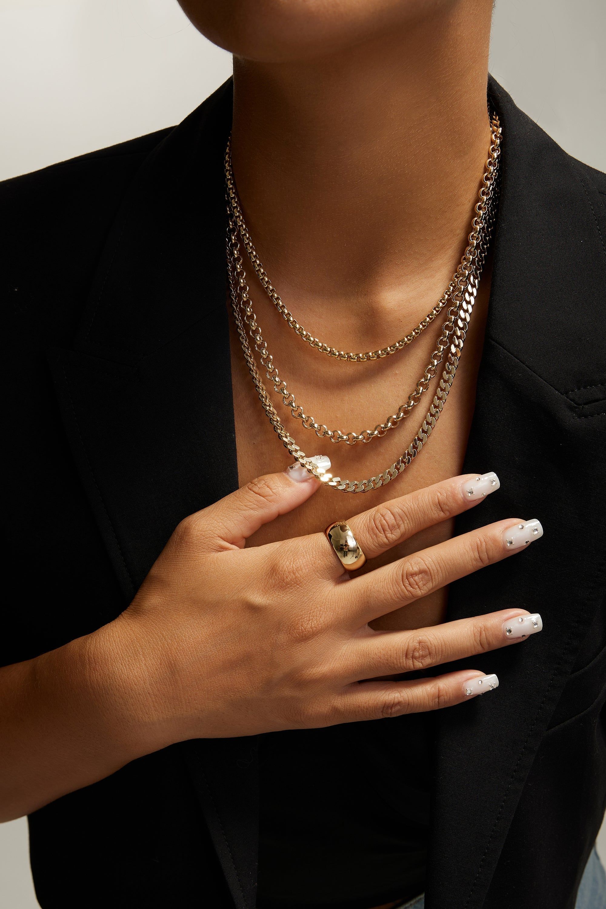 Woman’s hand with gold ring and layered gold necklaces showcasing Ludlow Triple Chain Necklace