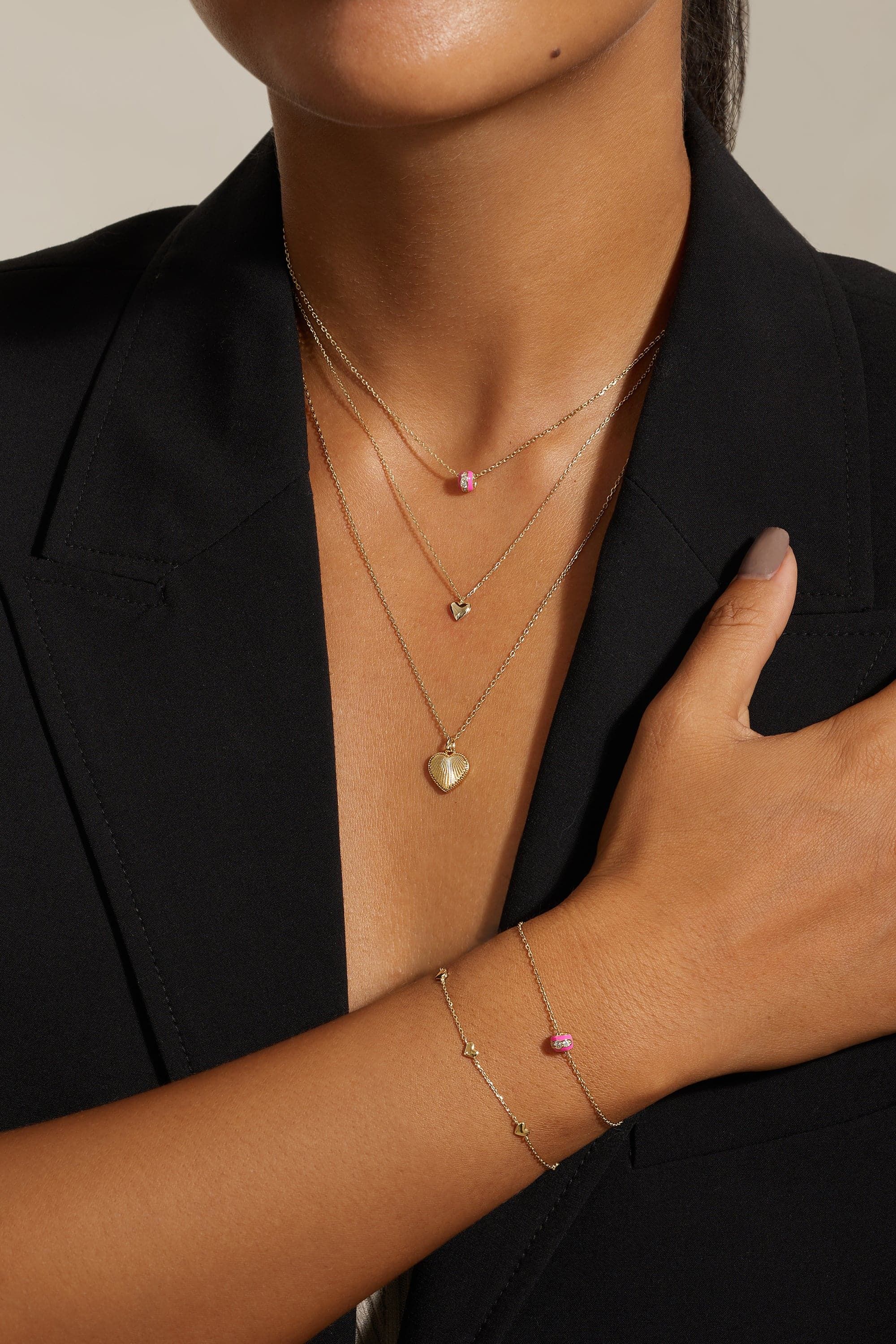 Woman wearing layered gold necklaces with pink beads and charms, and a Pink Enamel CZ Channel Rondelle Bracelet