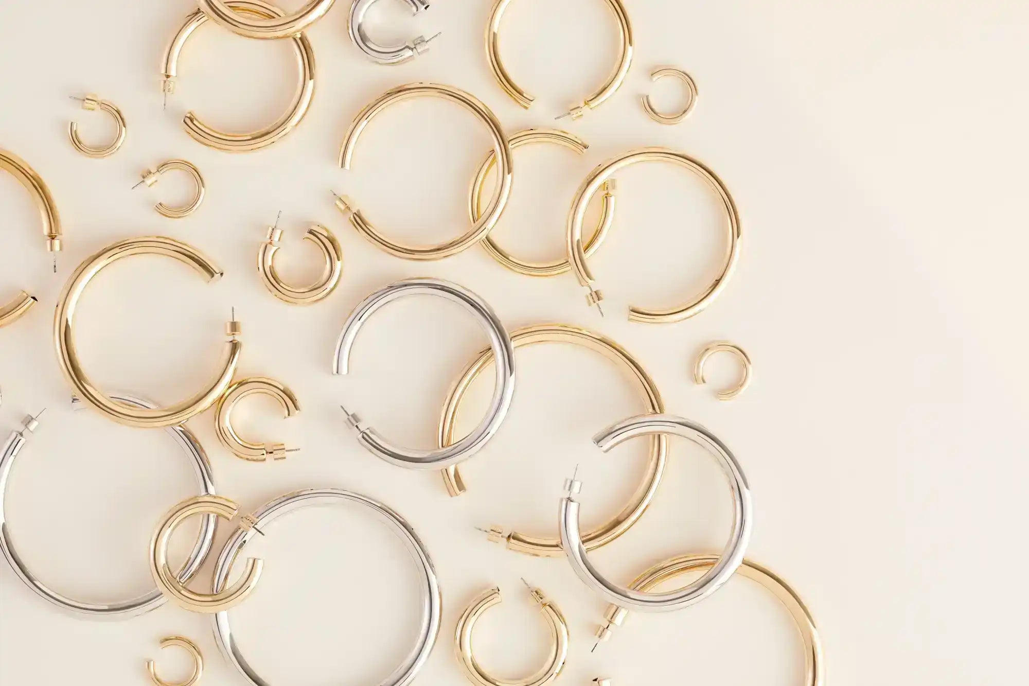 Collection of gold and silver hoop earrings on a light beige background