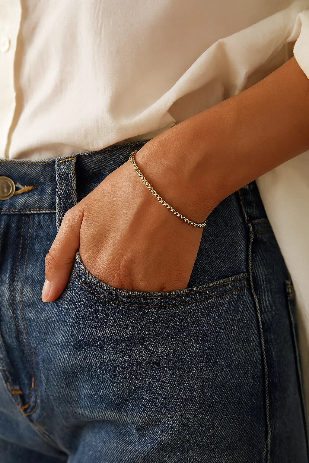 Thin Luciana Bracelet on person’s arm with blue jeans pocket, delicate gold-toned beads