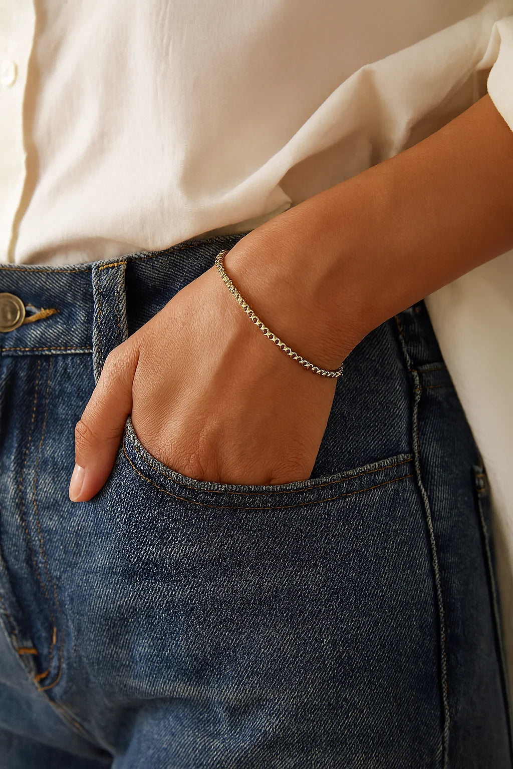 Thin Luciana Bracelet on person’s arm with blue jeans pocket, delicate gold-toned beads