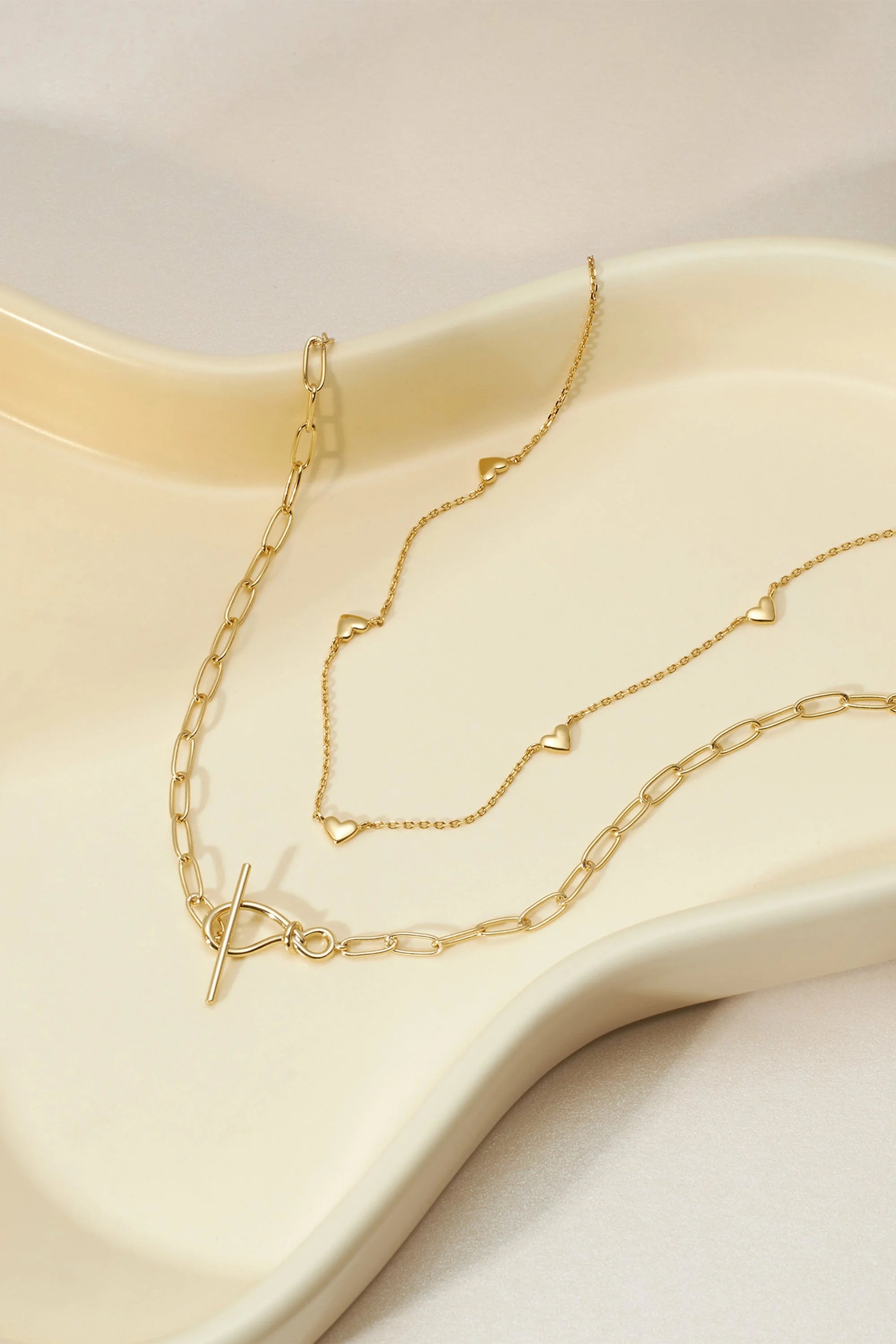 Two gold necklaces featuring knot toggle and paperclip chain styles