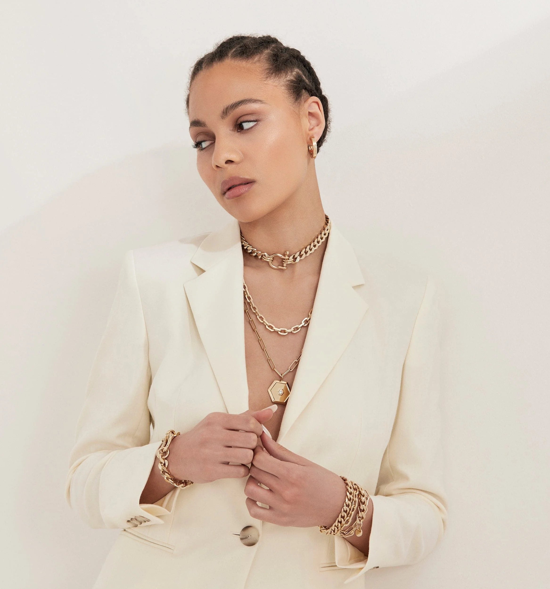 Woman wearing Lennon Necklace with gold jewelry and white blazer in a stylish setting