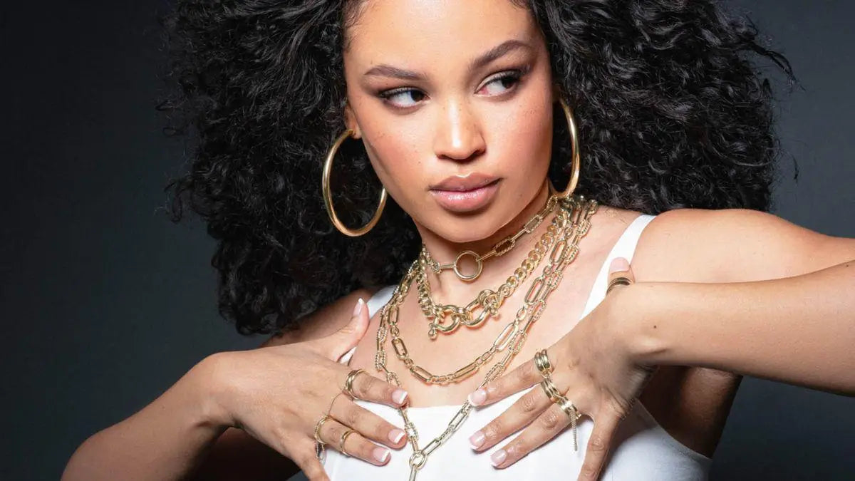 Woman showcasing elegant gold jewelry including a link chain and chain bracelet.