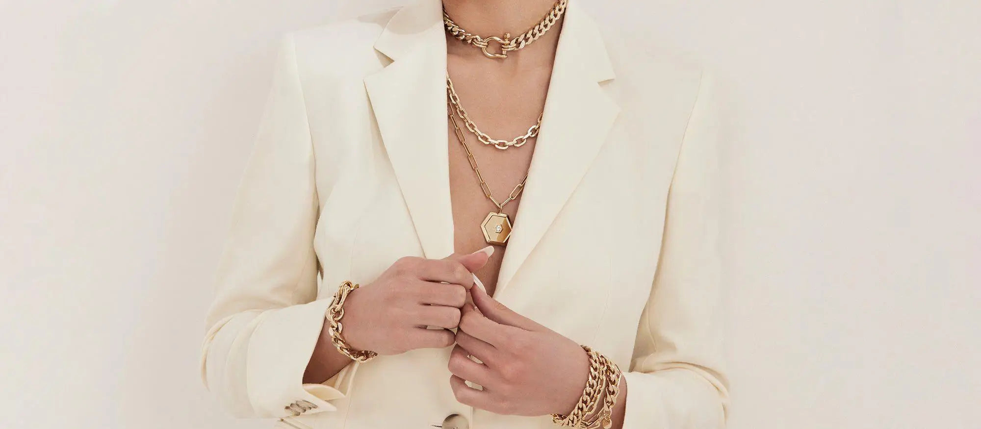 Woman wearing gold jewelry and a white blazer showcasing elegant charm necklaces