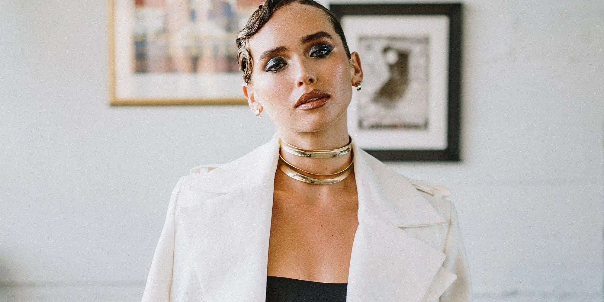 Woman wearing a white jacket and gold necklaces, highlighting stylish choker necklace color.