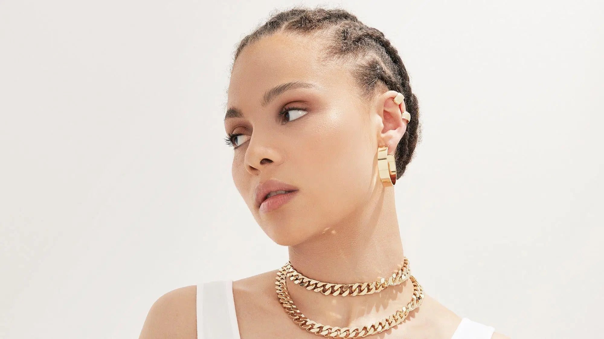 Woman with braided hair showcasing trendy ear cuffs and gold jewelry in stylish designs.