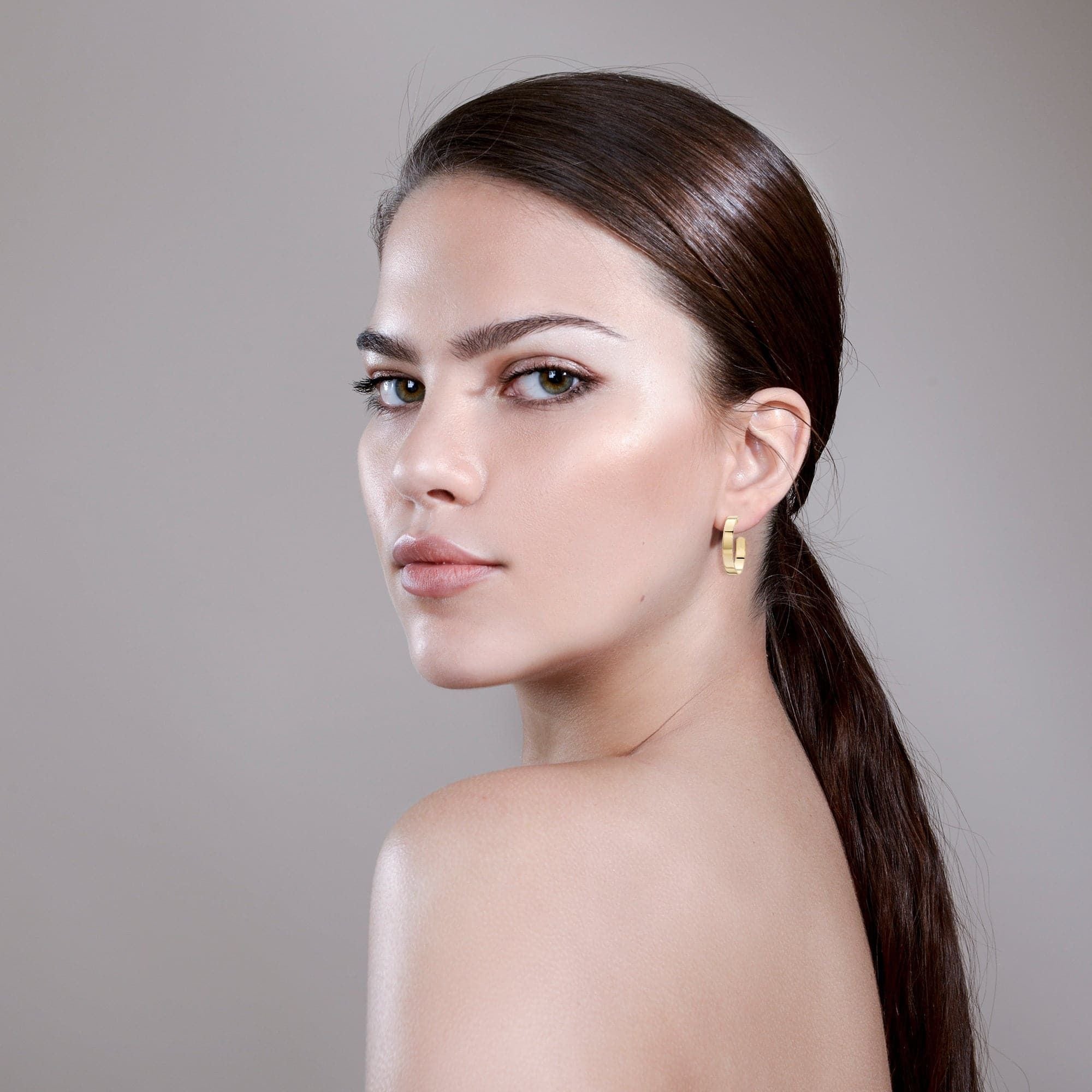 Woman with sleek hair and gold earrings showcasing wide flat recycled brass Isla Hoops