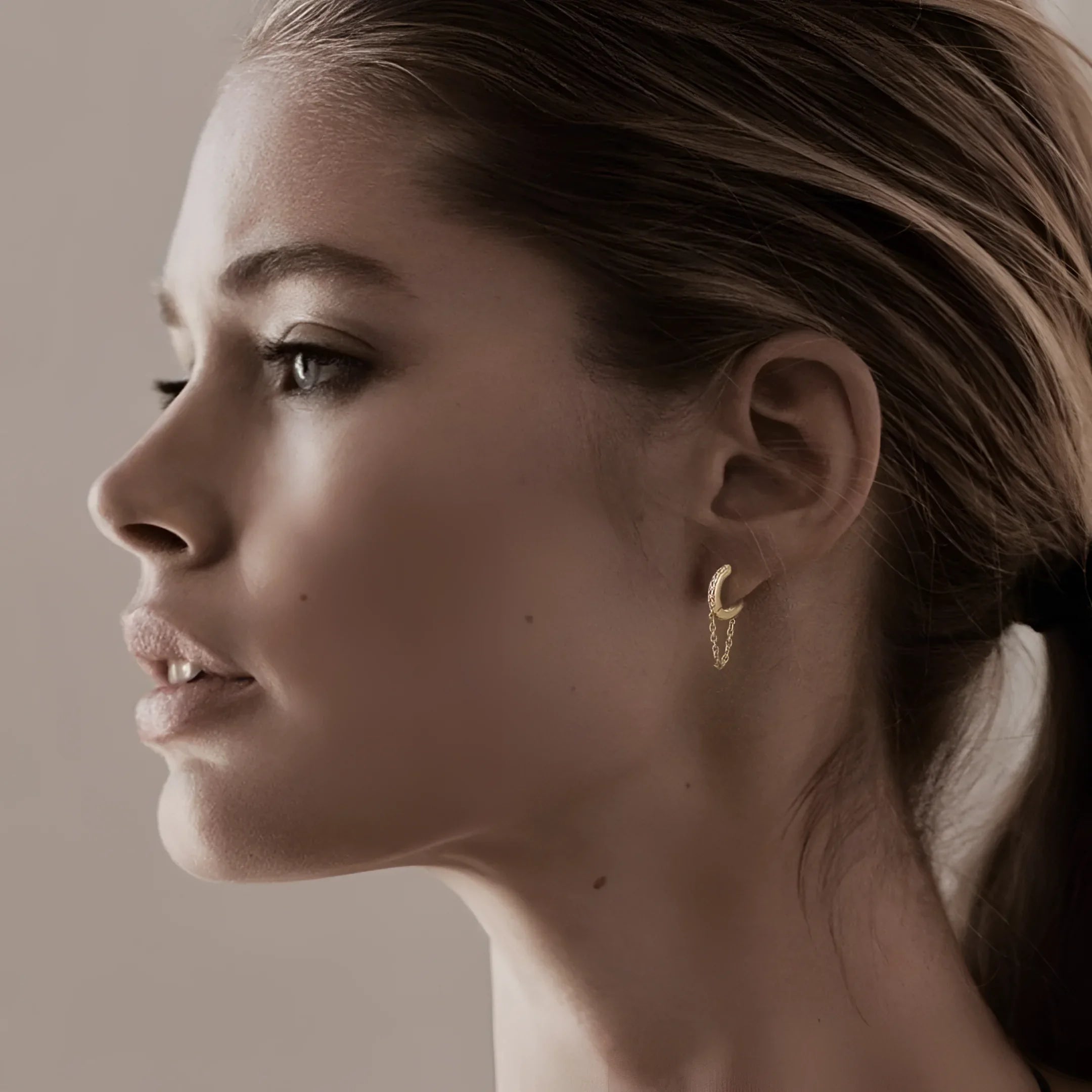 Woman showcasing 10Mm Diamond and 14K solid yellow gold huggies with a yellow gold chain