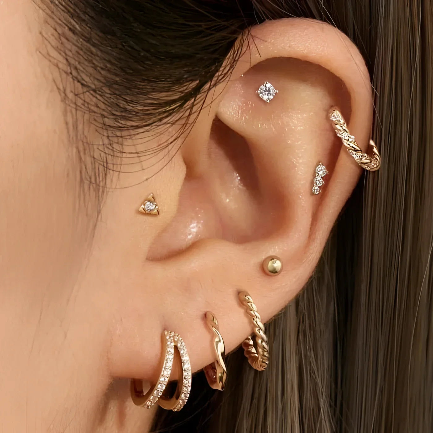 Ear with multiple gold-toned piercings featuring 14K Solid Yellow Gold diamond twisted huggie hoops