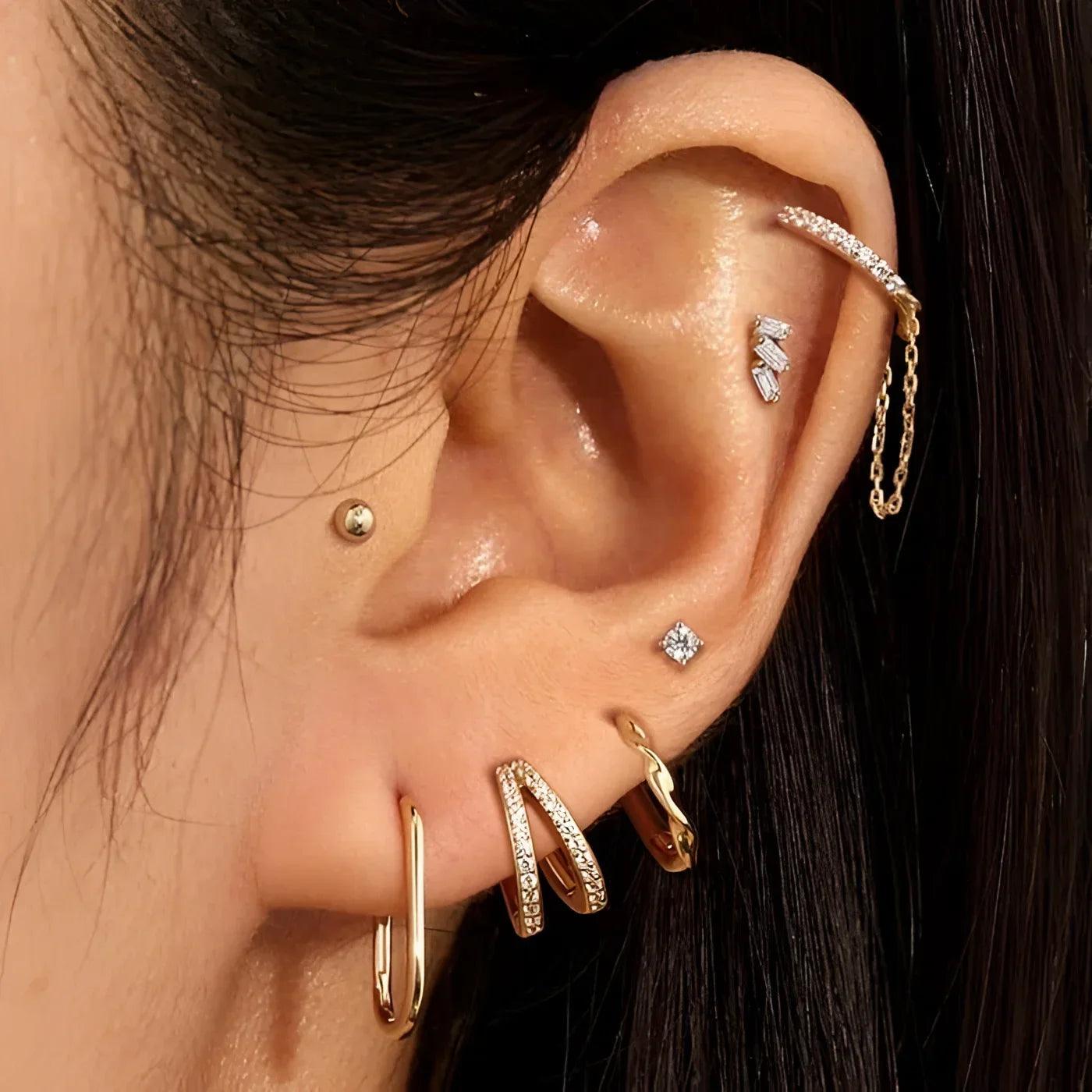 Ear with multiple gold and jeweled piercings featuring 14K solid yellow gold oval hoops