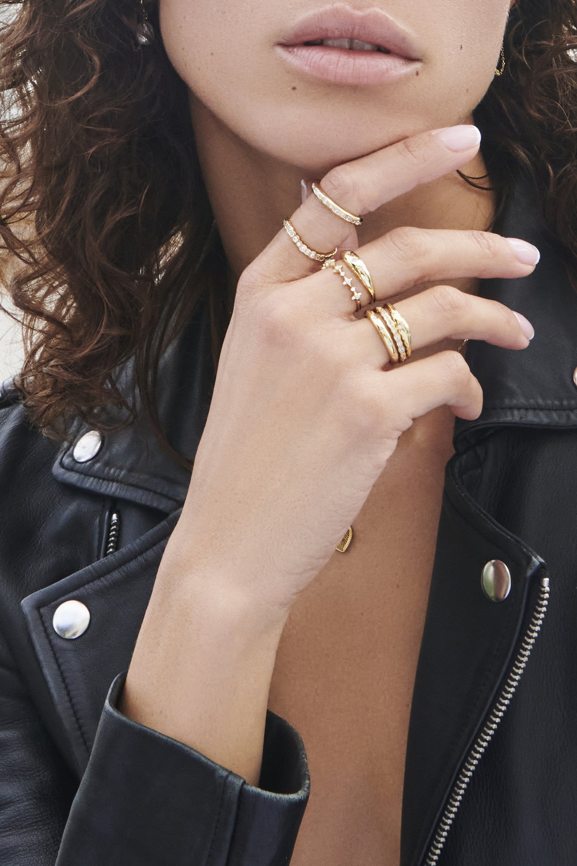 a woman wearing a black leather jacket and gold rings