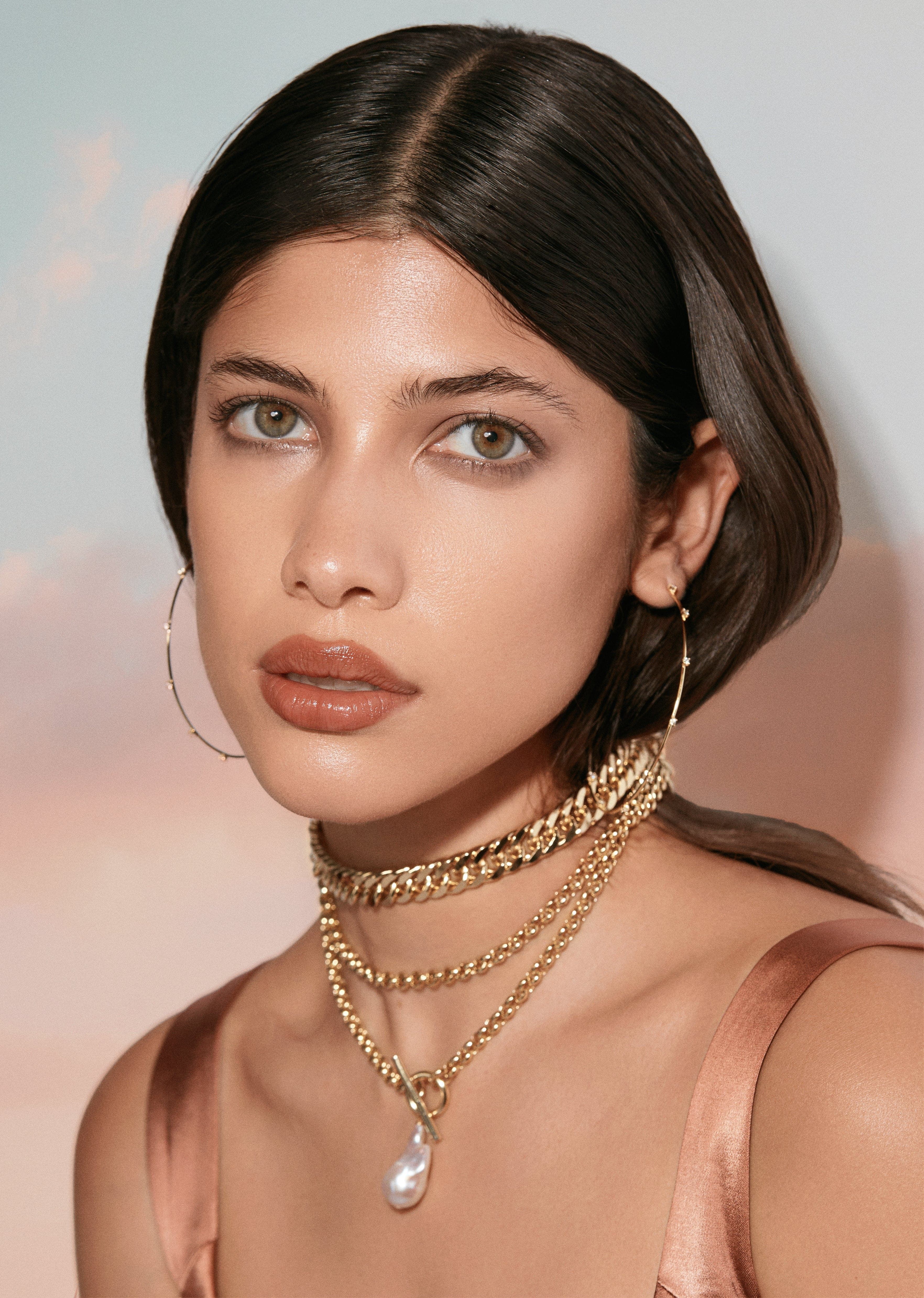 a woman wearing a gold choker and a pearl necklace