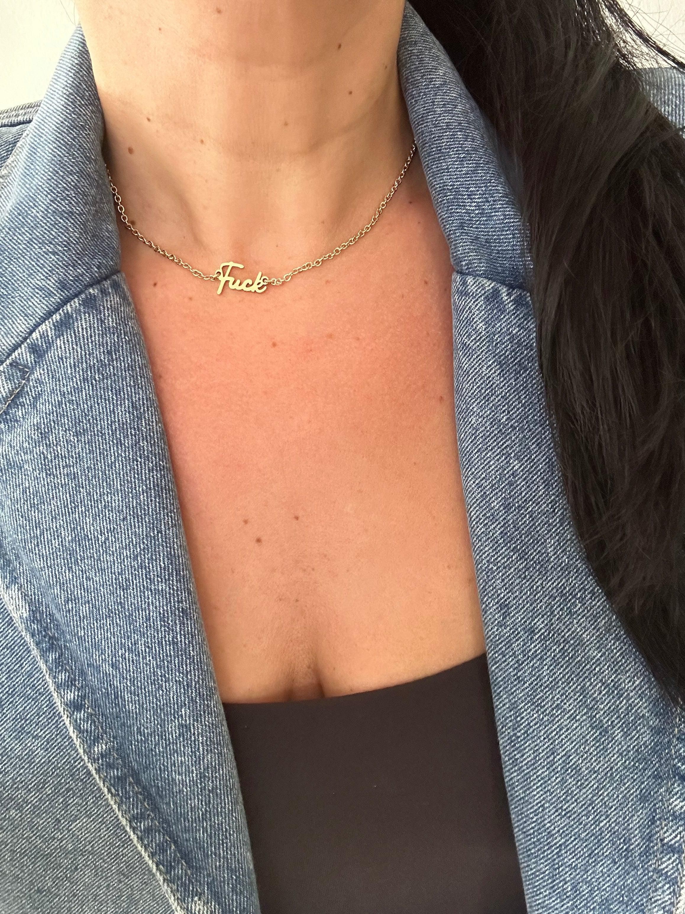 Woman wearing Dainty Script Fuck necklace in gold, styled with a denim jacket and black top.