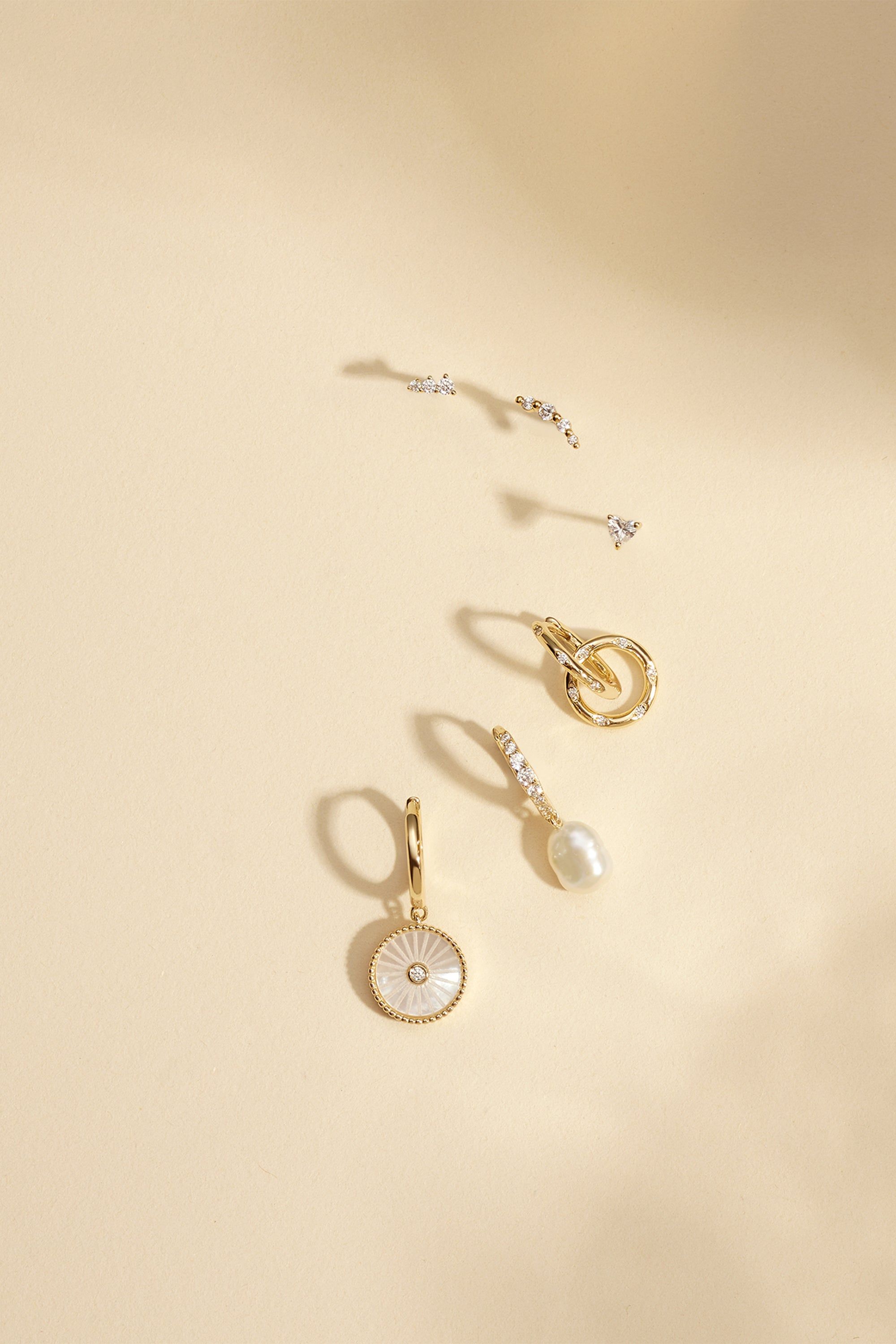 three pairs of earrings on a beige surface