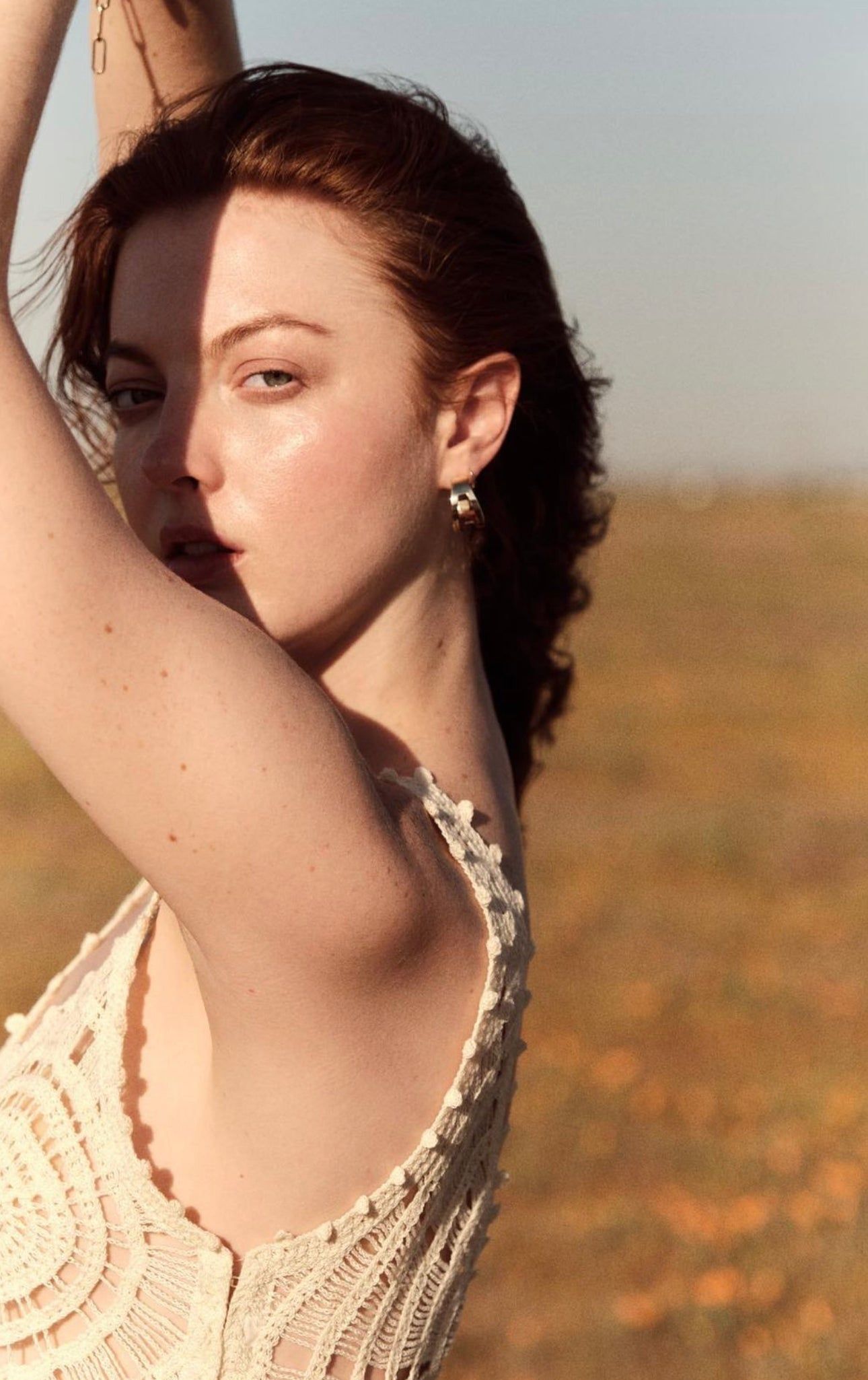 a woman standing in a field with her arms behind her head