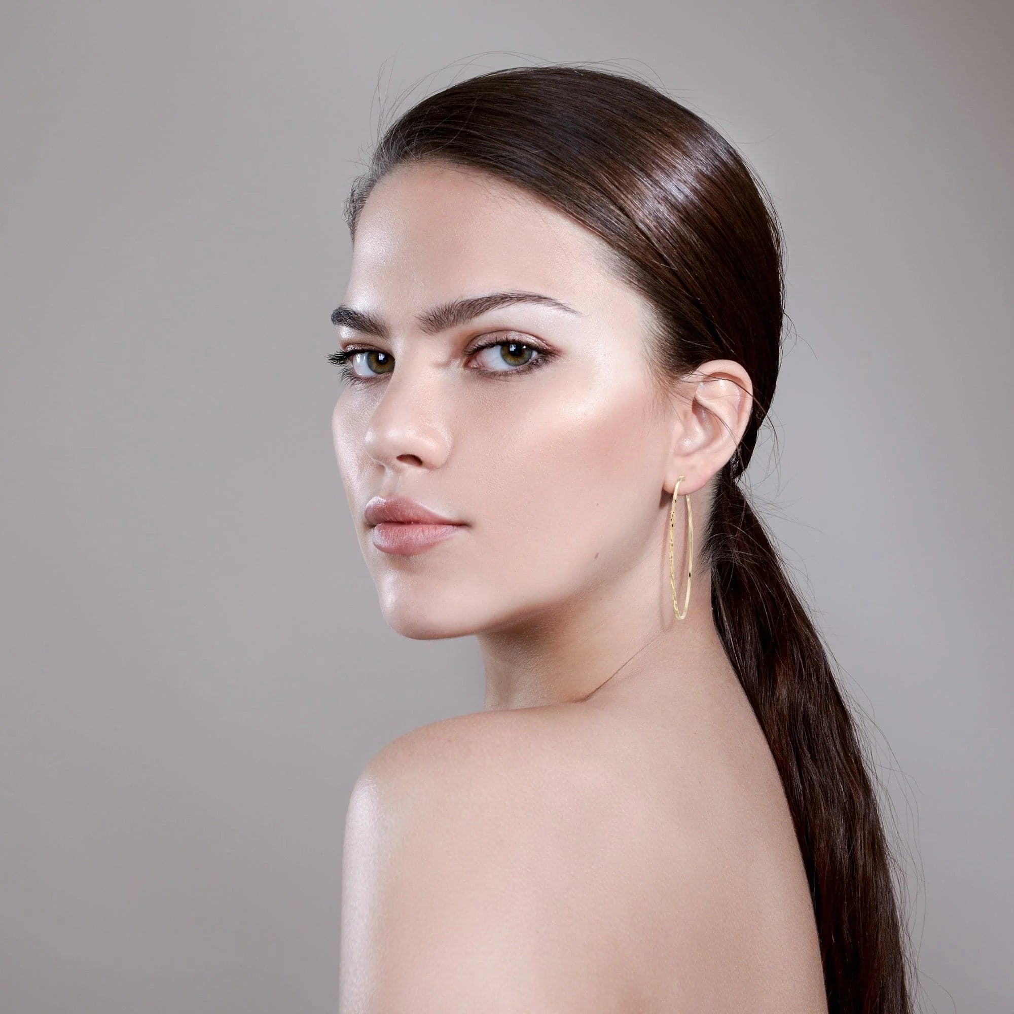 Woman with sleek hair wearing Avery Hoops earrings made from recycled brass and hoop measures