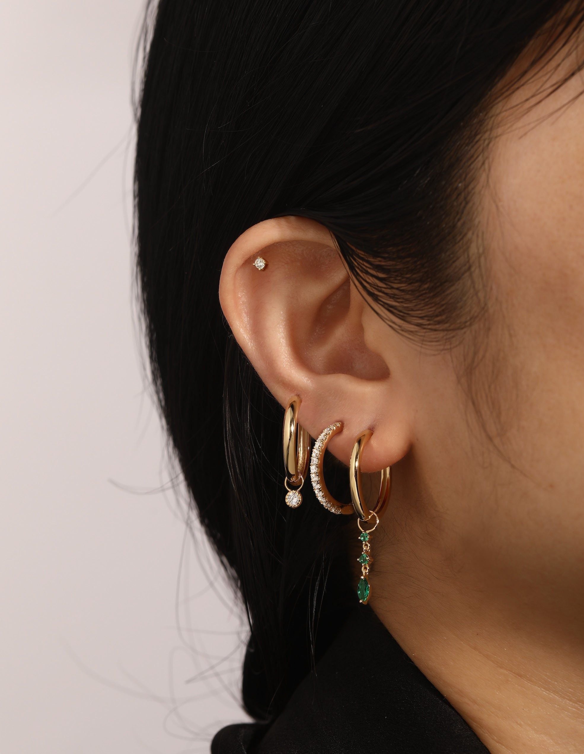 Ear adorned with Cz Solitaire Hoop Charm and multiple 14k gold vermeil earrings