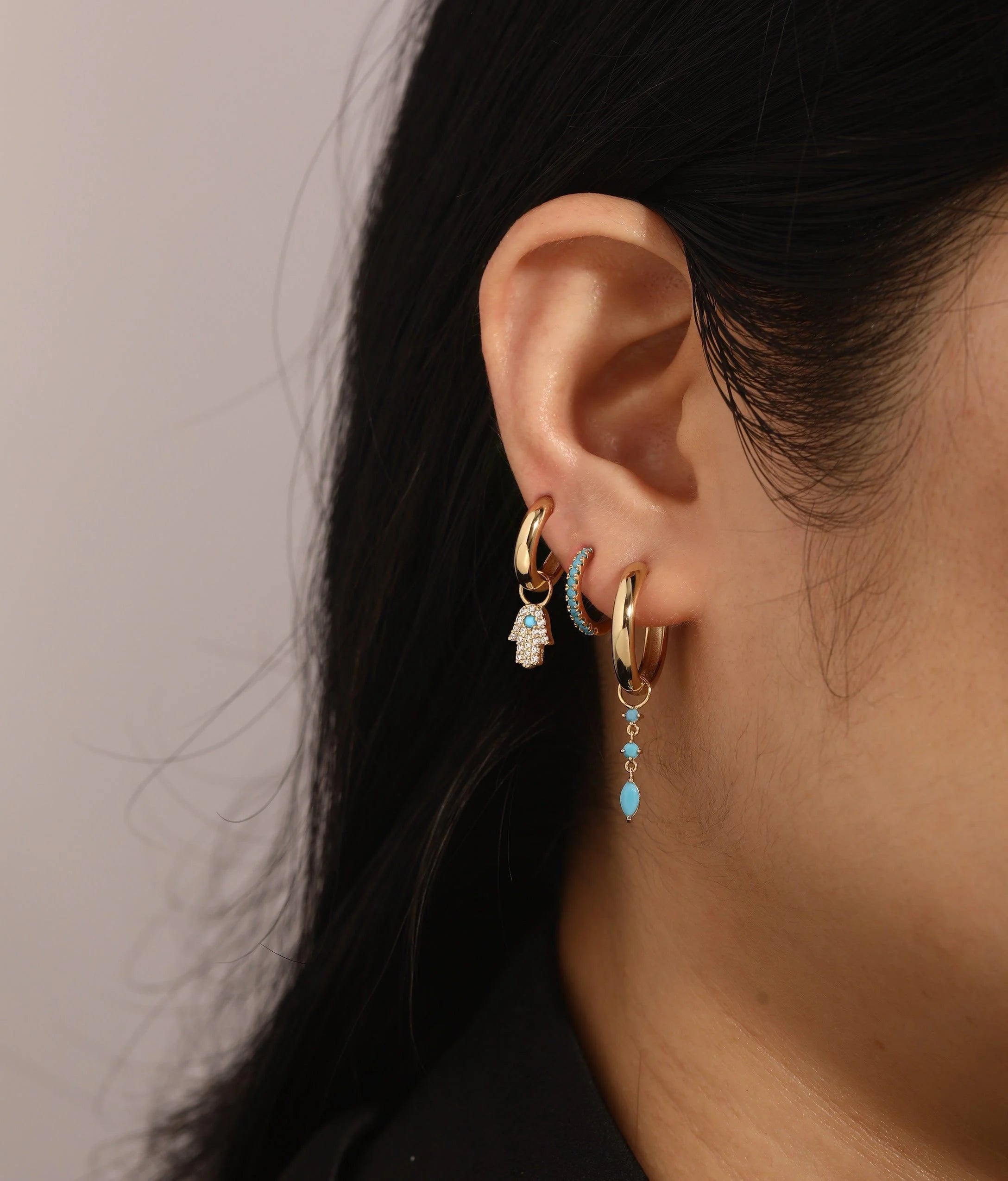 Ear with multiple gold hoop earrings showcasing CZ & Turquoise Hamsa Hoop Charm