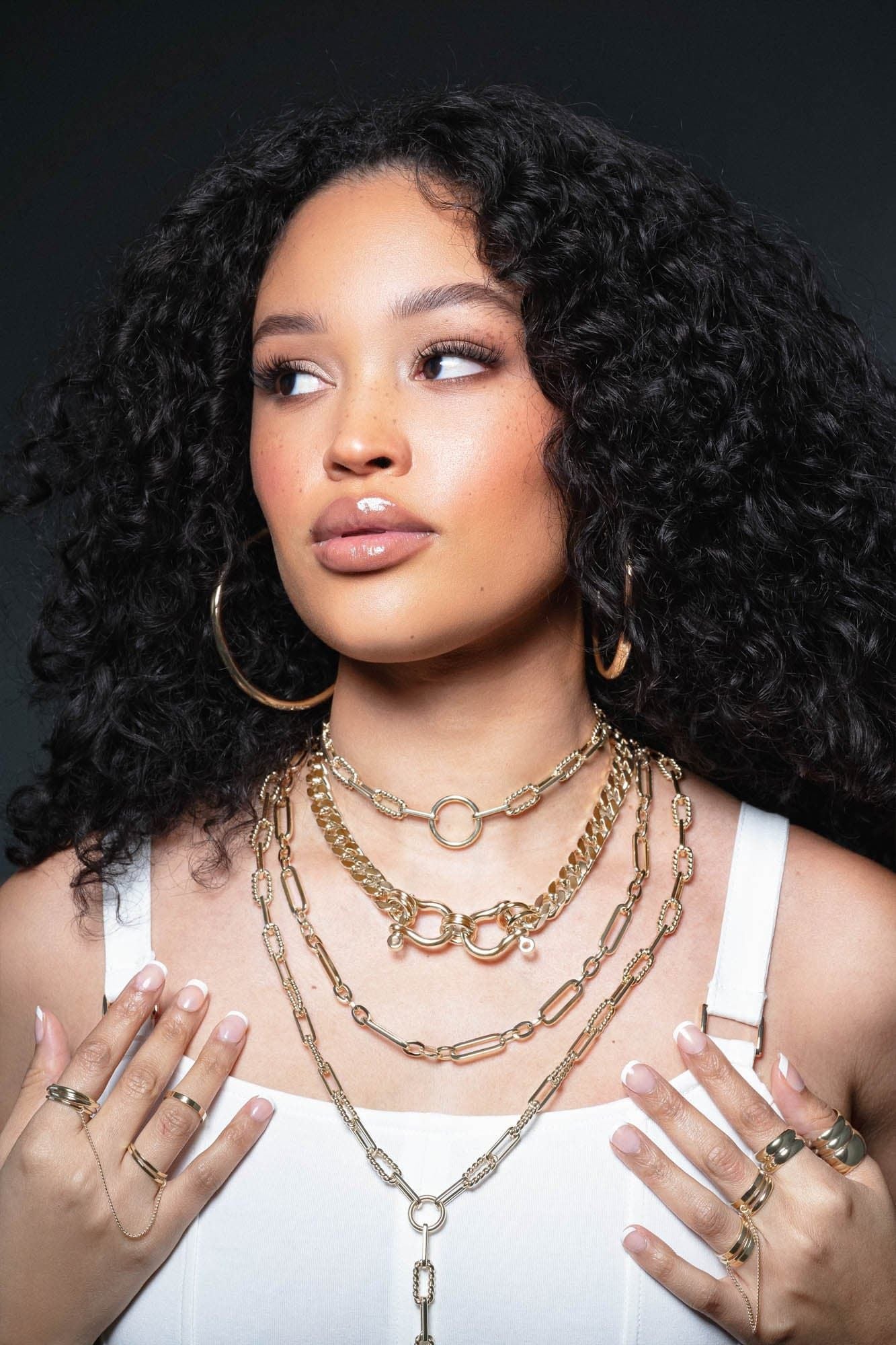 Woman showcasing layered gold necklaces and rings with a double domed ring