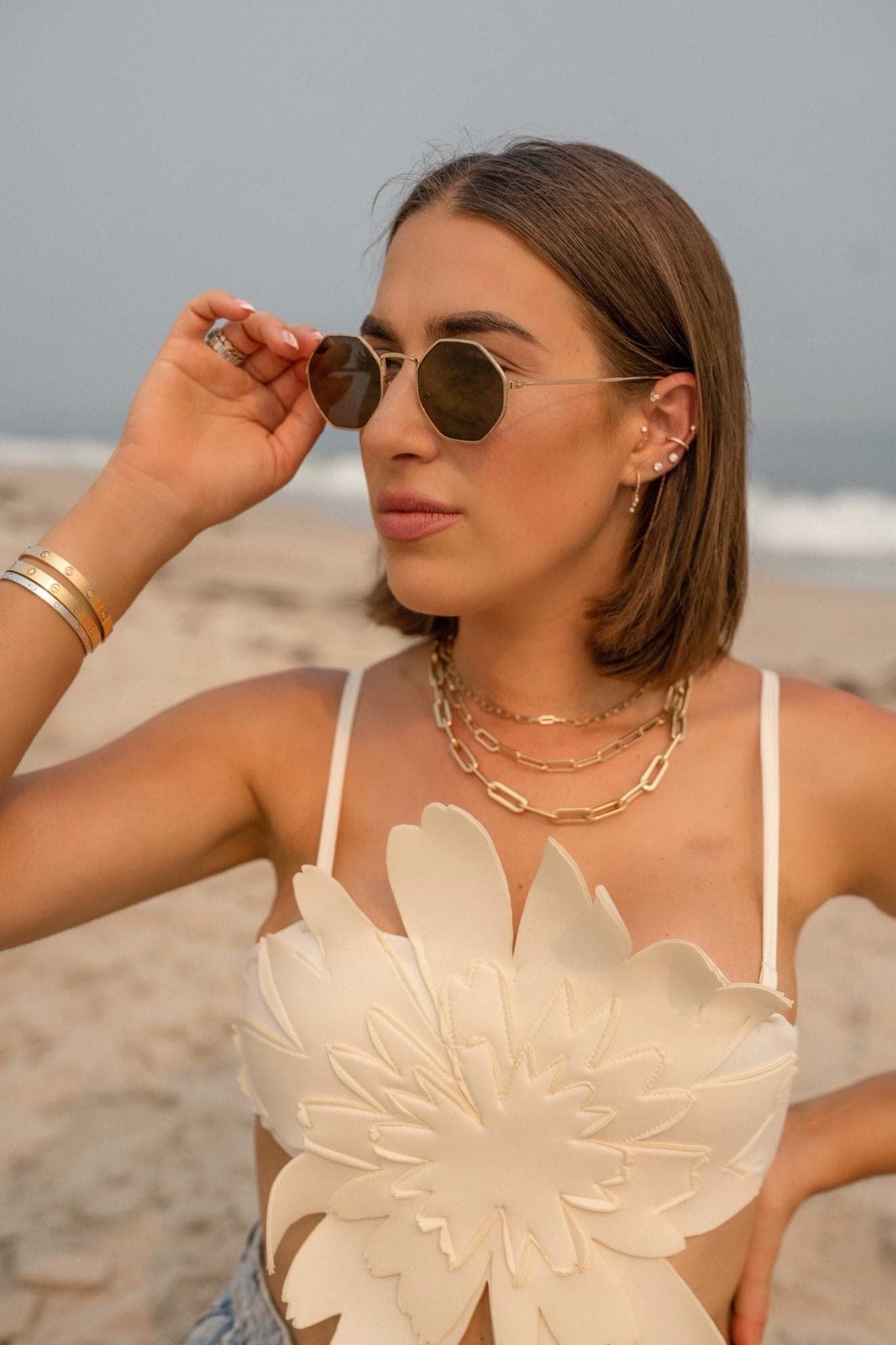 Woman in sunglasses and floral top showcasing the Dr. Bridget Necklace, plated 14k gold