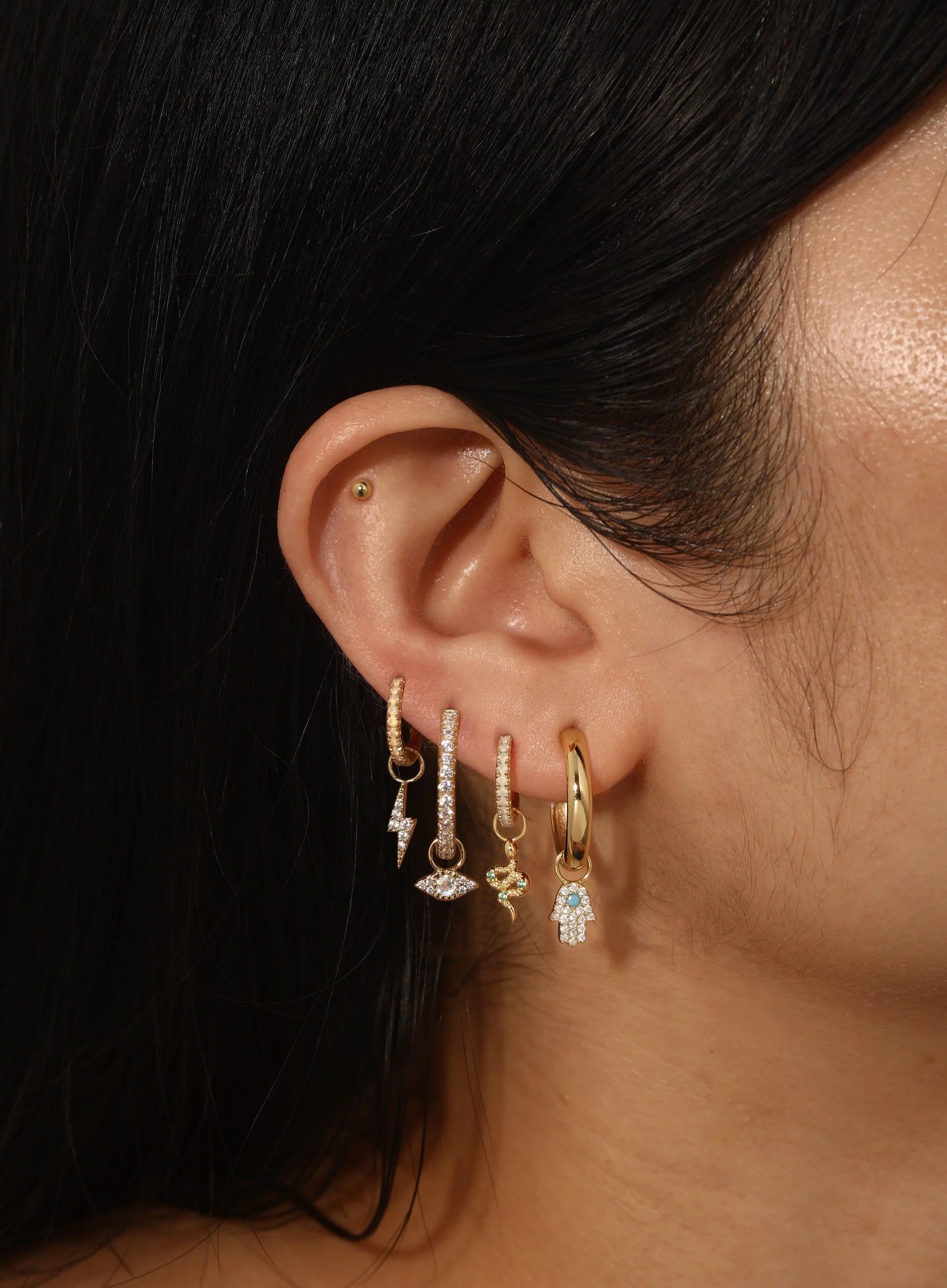 Ear with multiple gold earrings showcasing CZ Snake Hoop Charm from Demi-Fine Collection Earrings