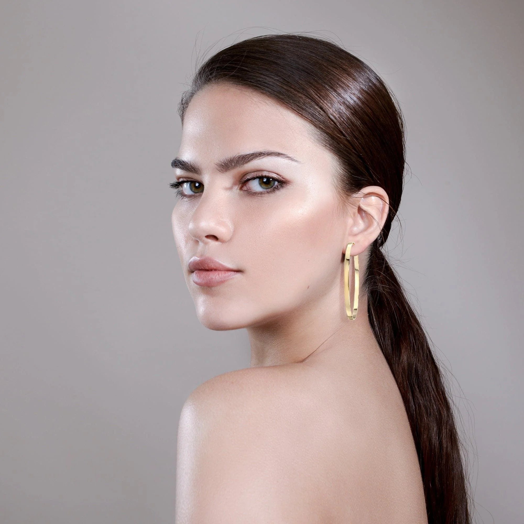 Woman showing off stylish 2.5 inch Isla Hoops gold earrings