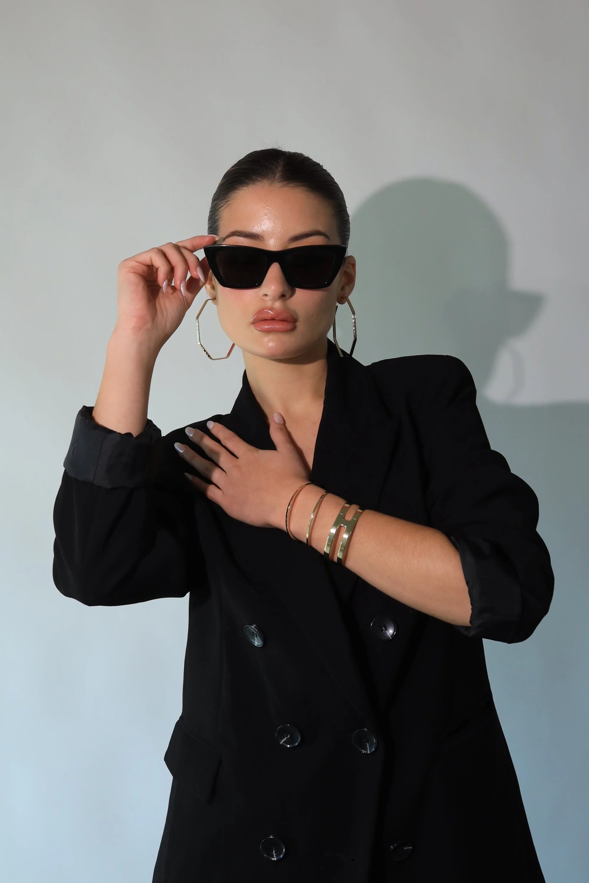 Fashionable woman in black blazer and sunglasses wears rectangle cut-out cuff bracelet