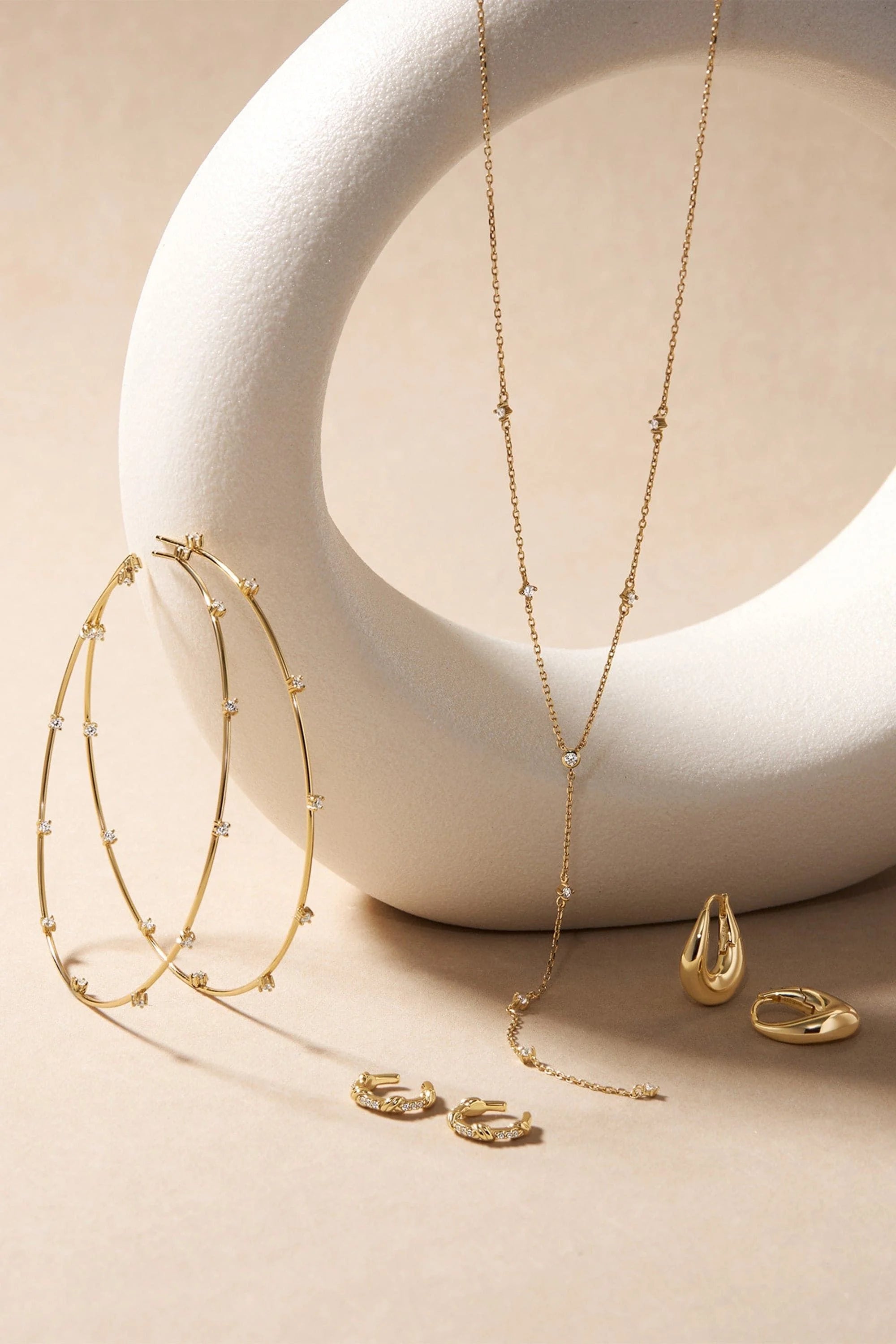 Gold jewelry collection with diamond accents including hoop earrings, lariat necklace, and rings