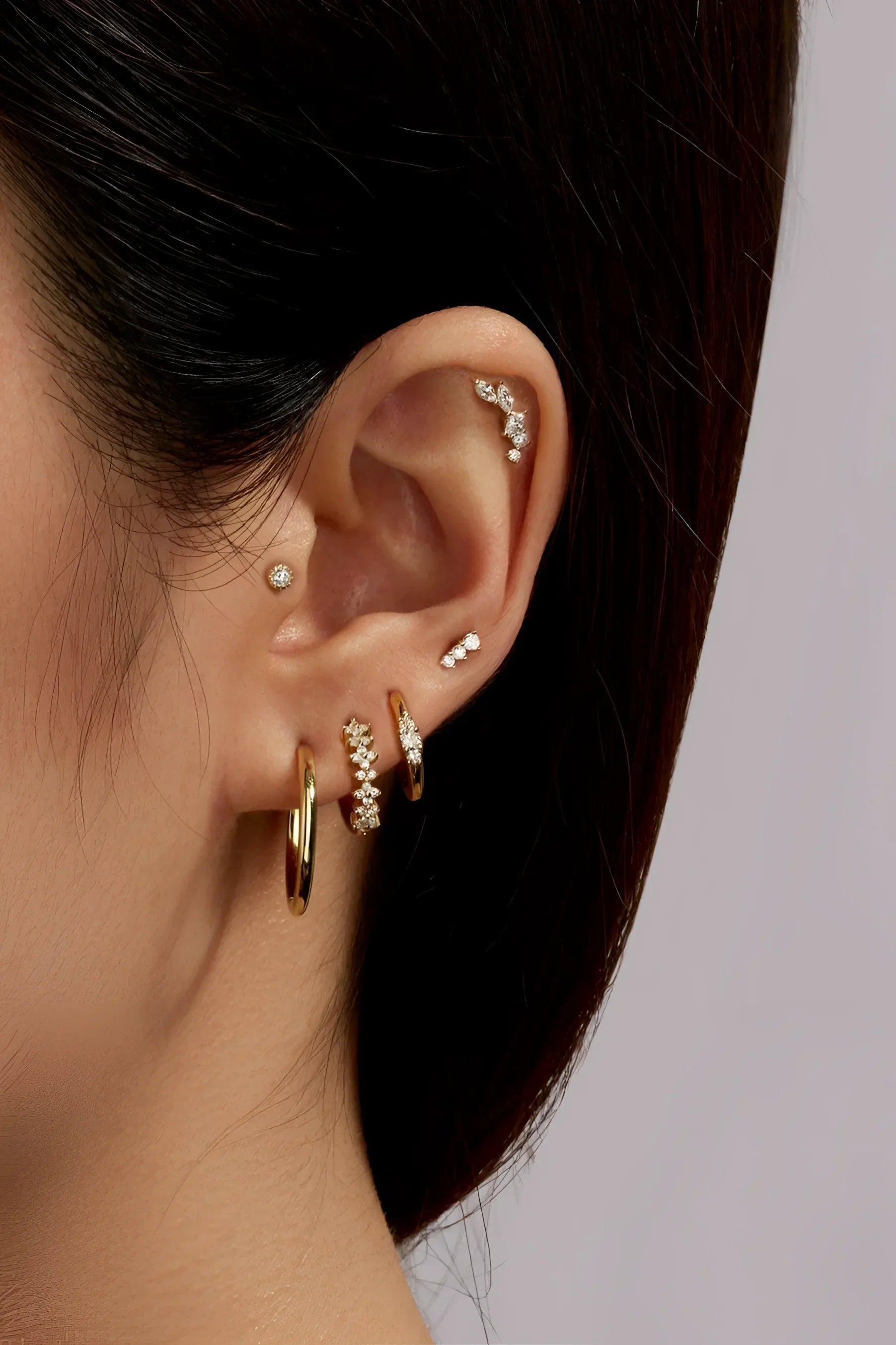 Ear with multiple gold and jeweled earrings from the Triple CZ Stone Earrings collection