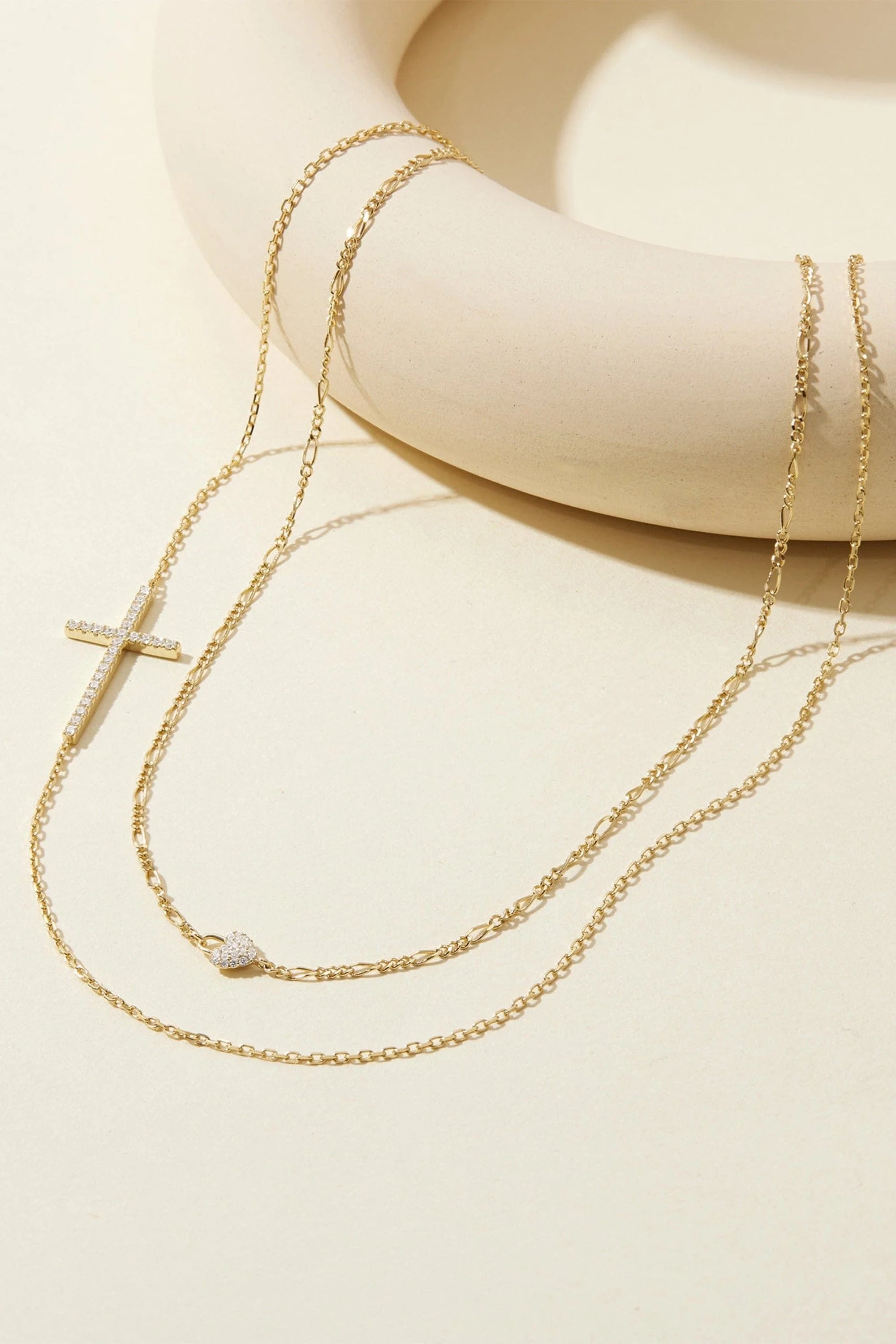 Gold-toned layered necklace with pave rhinestone cross pendant and delicate heart charm