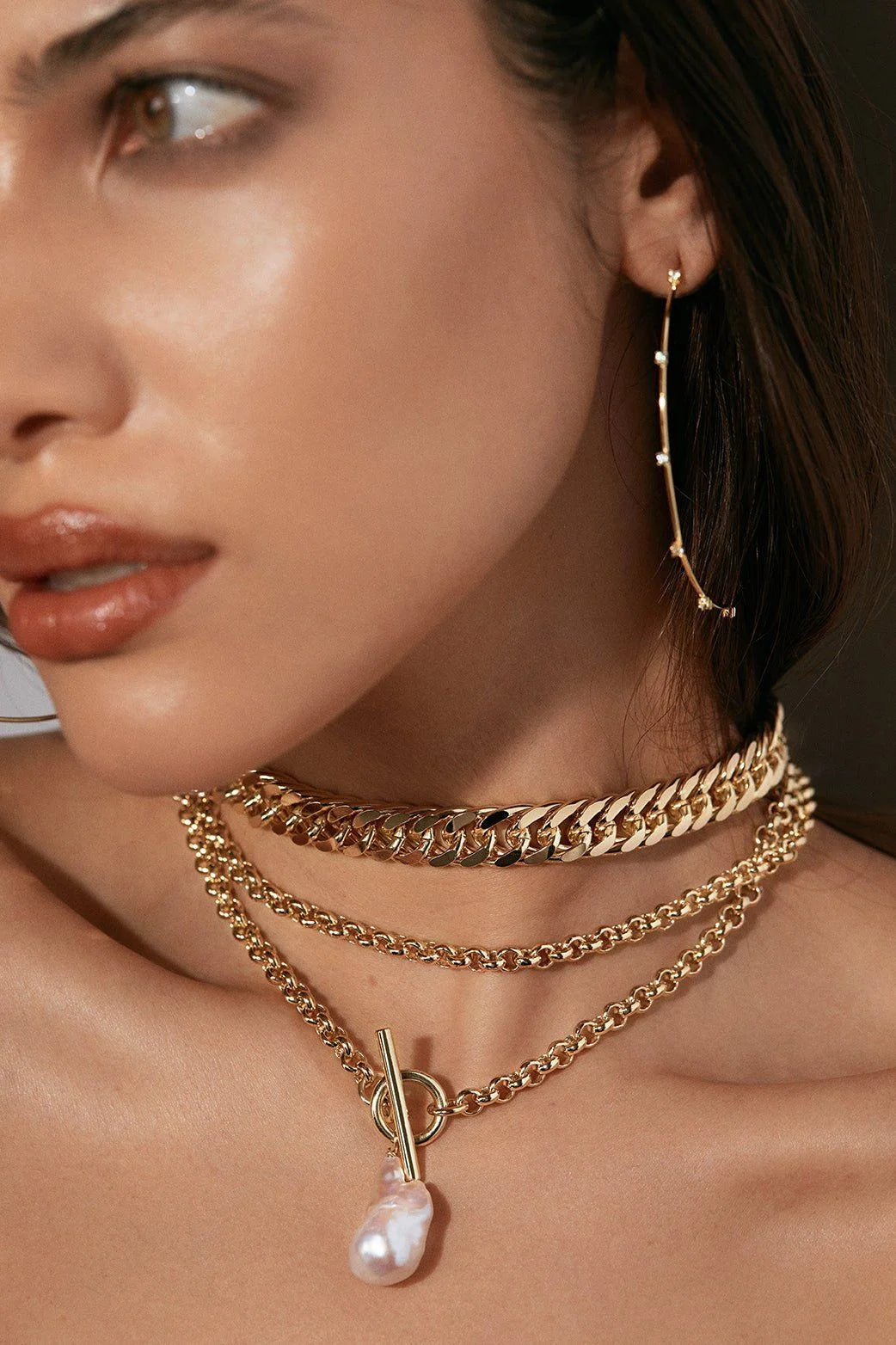 Woman wearing layered gold necklaces and a dangling earring with the Micro Royal Toggle Pendant