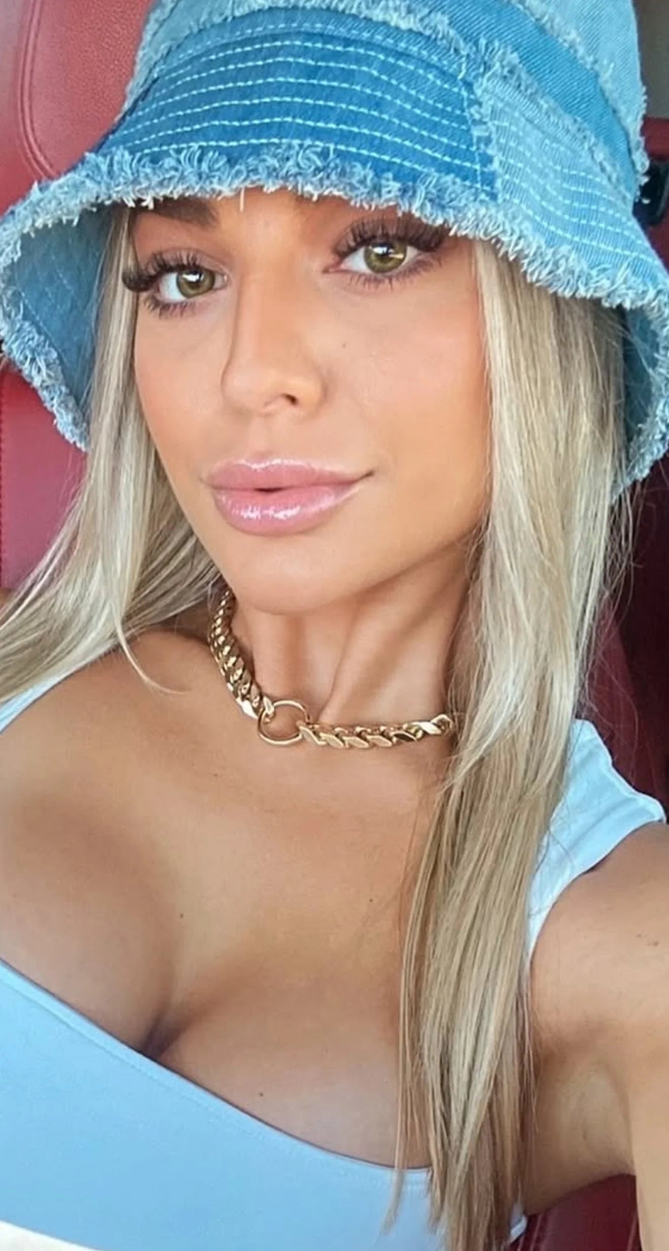 Woman with long blonde hair wearing a light blue top gold chain necklace and denim bucket hat
