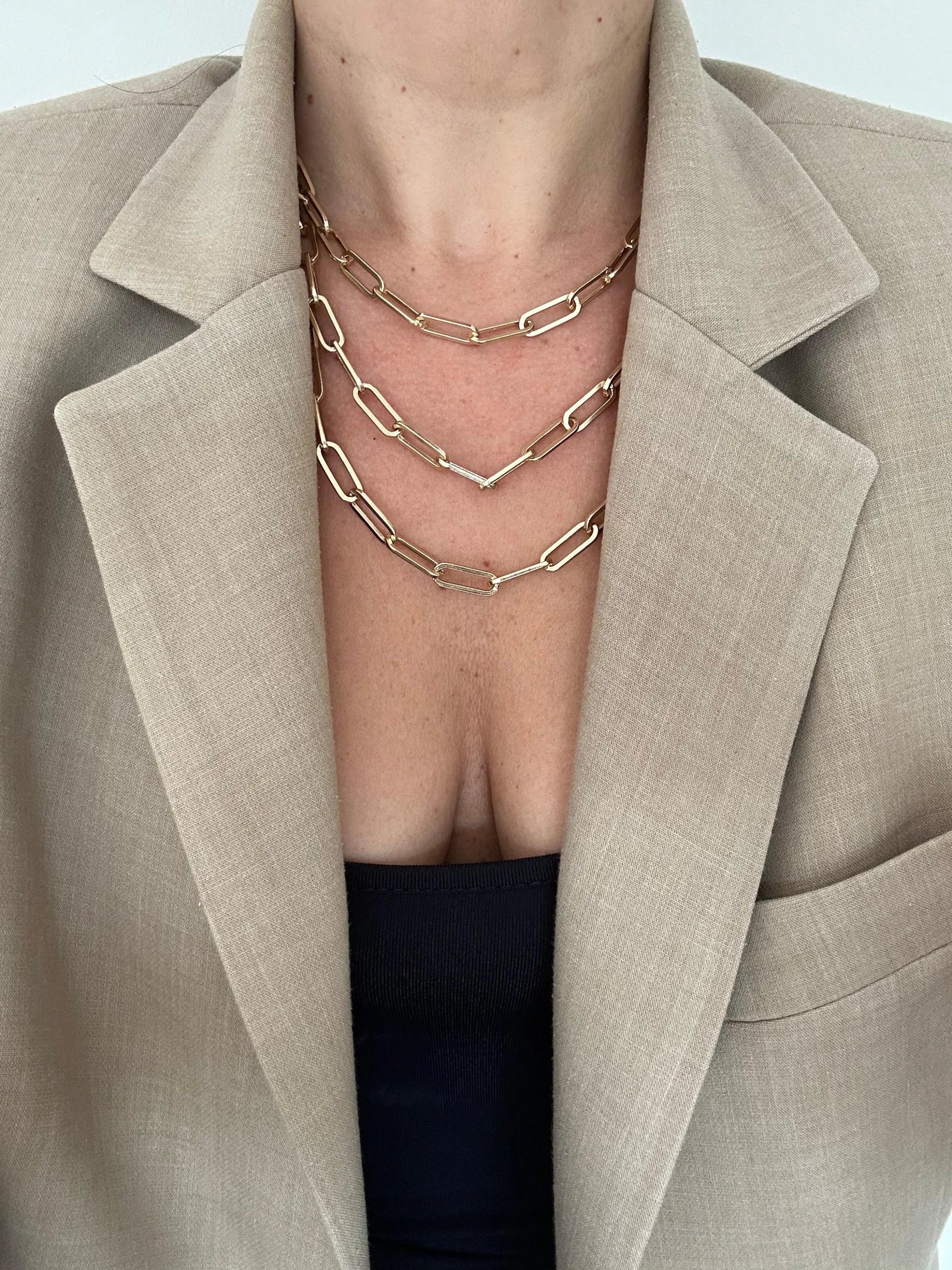 Layered gold chain necklaces on a woman in a blazer showcasing the Triple Large Elongated Link Chain Necklace