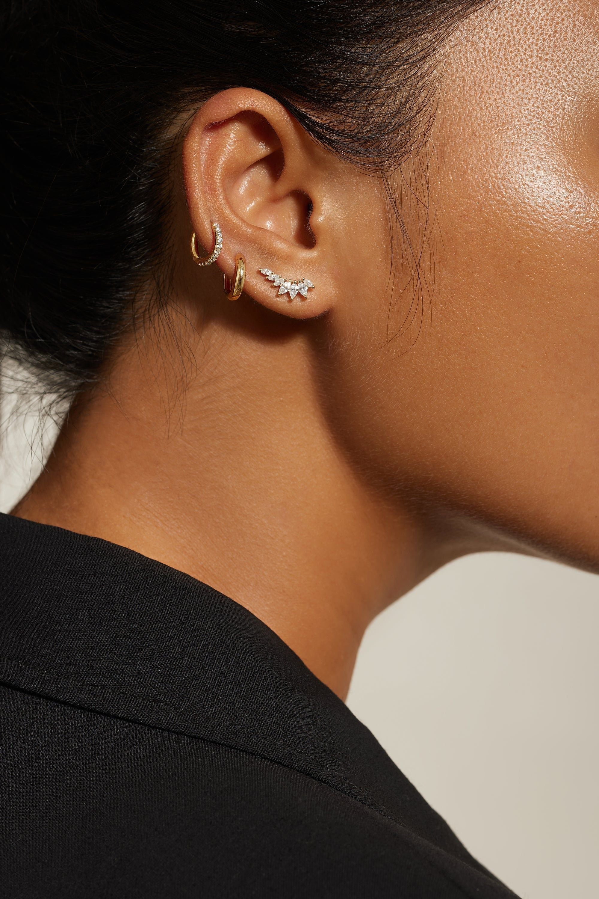 Ear adorned with multiple jewelry pieces featuring a Graduated Marquis Shaped Cz Ear Crawl