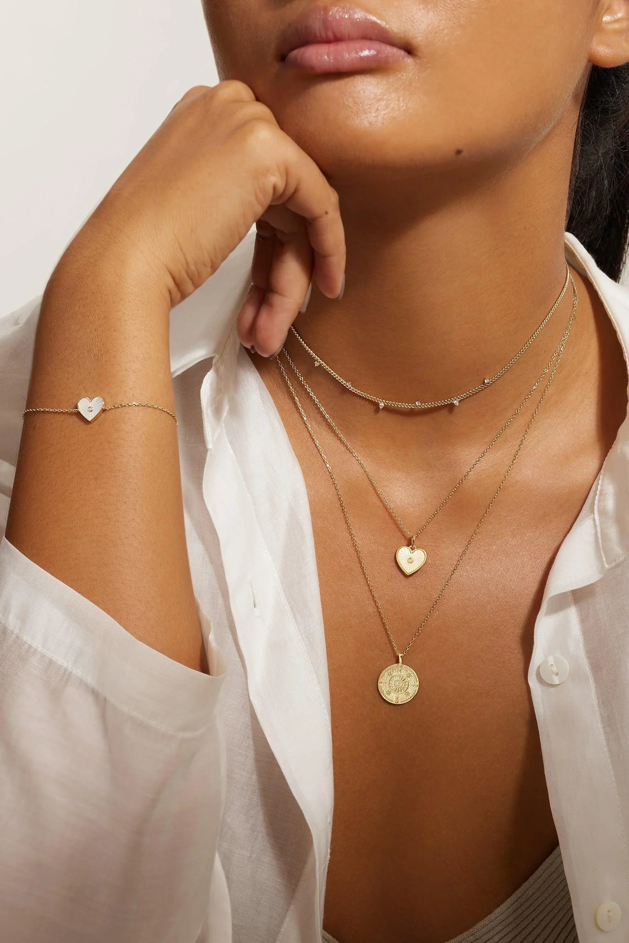 Woman wearing layered gold necklaces and a heart-shaped bracelet with CZ stone