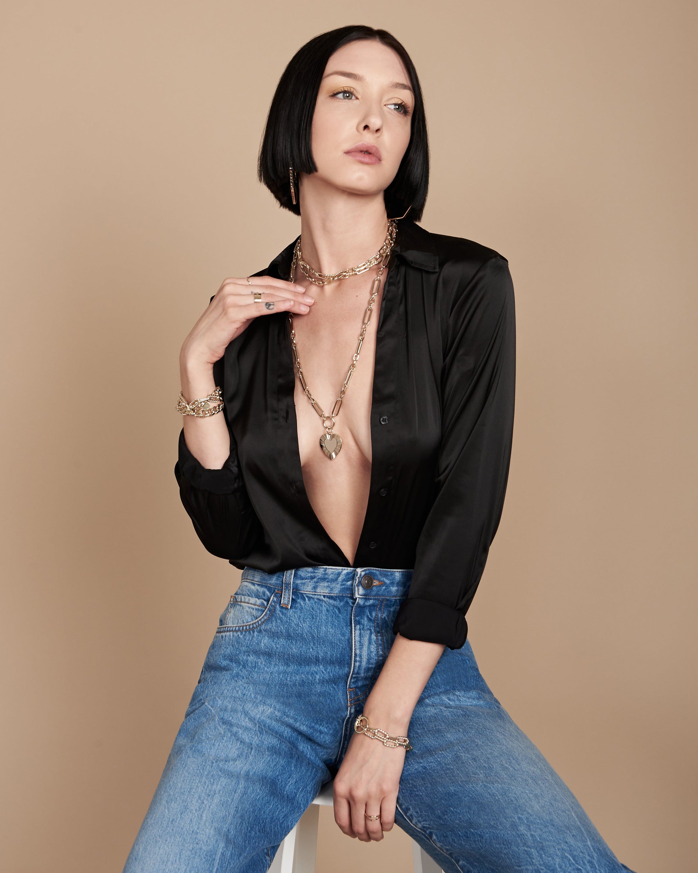 Woman in black blouse and jeans wearing the Hildegard Pendant with brass plated 14k gold