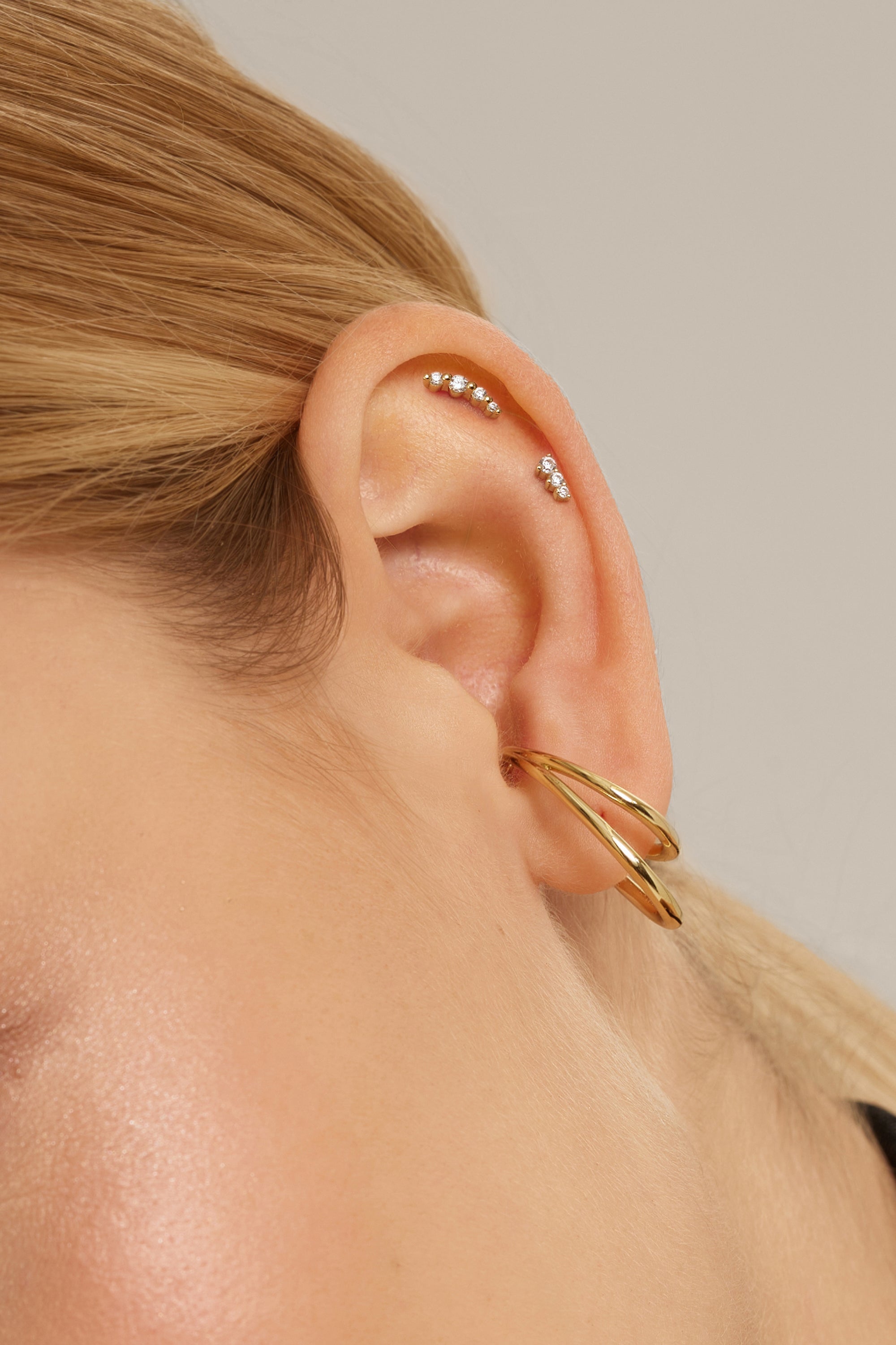 Ear showcasing a large dual ear cuff with multiple gold-colored piercings