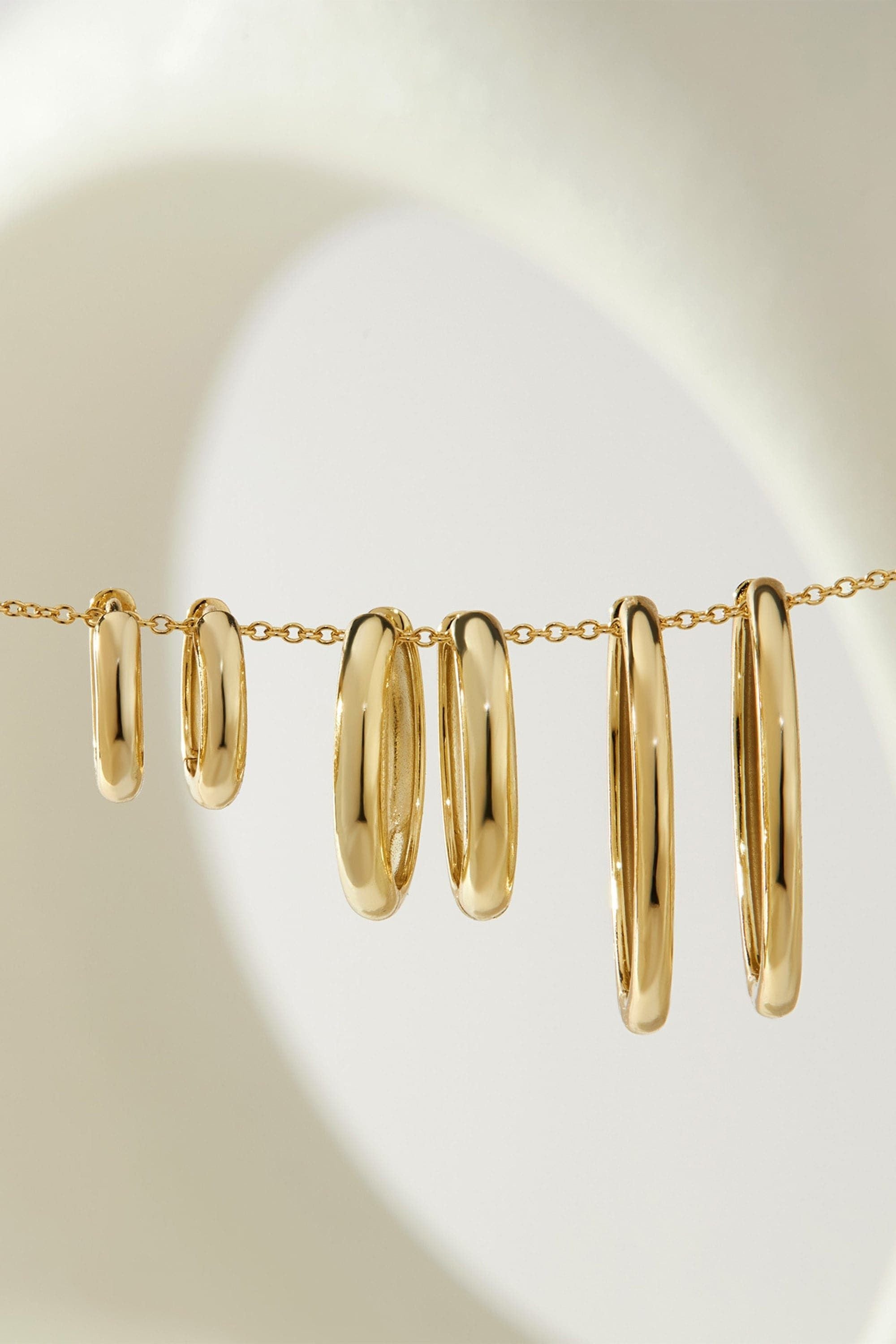 Gold hoop earrings on a chain, featuring 14k gold plated medium huggie hoop design