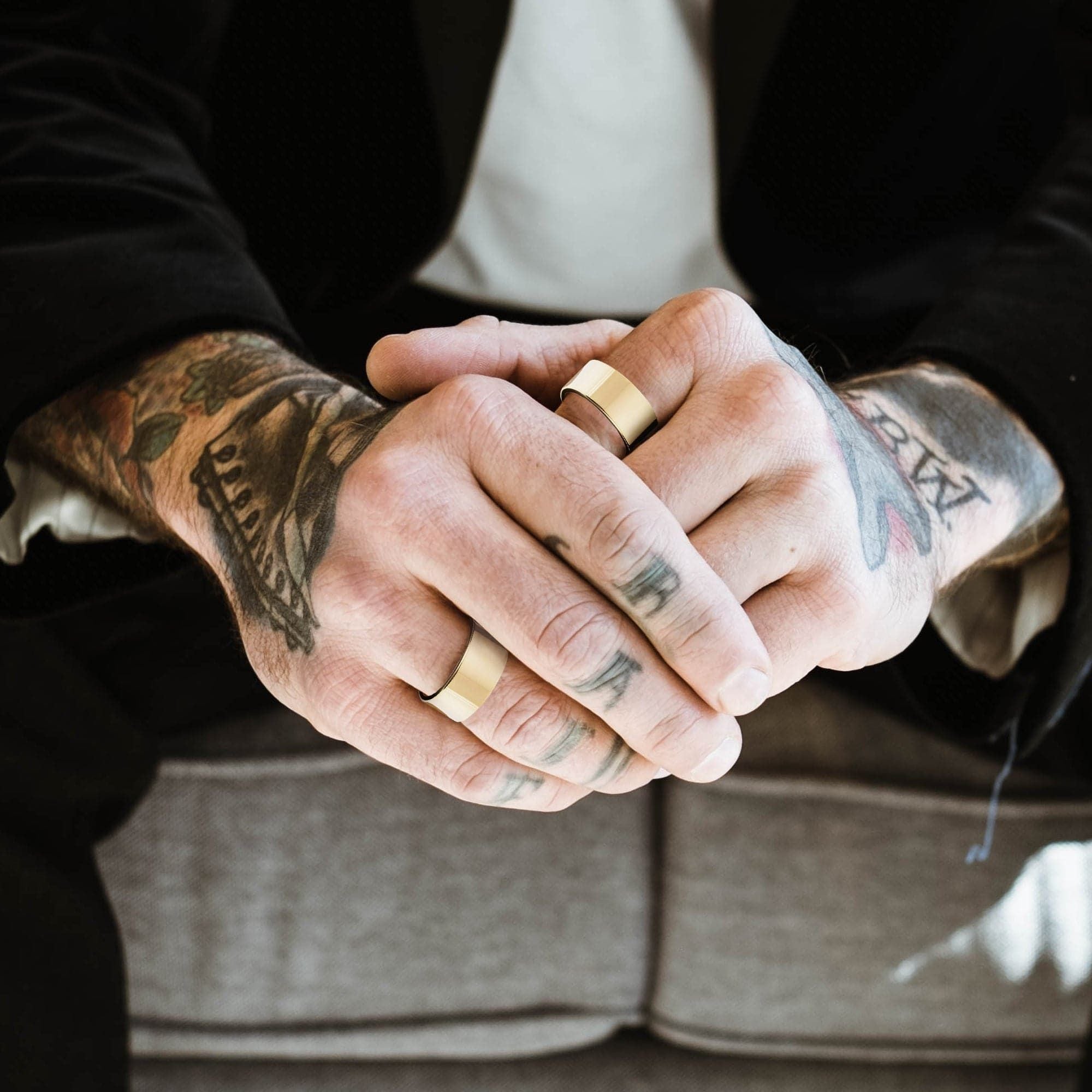 Tattooed hands wearing gold rings showcasing a Men’s 9.5mm flat ring design