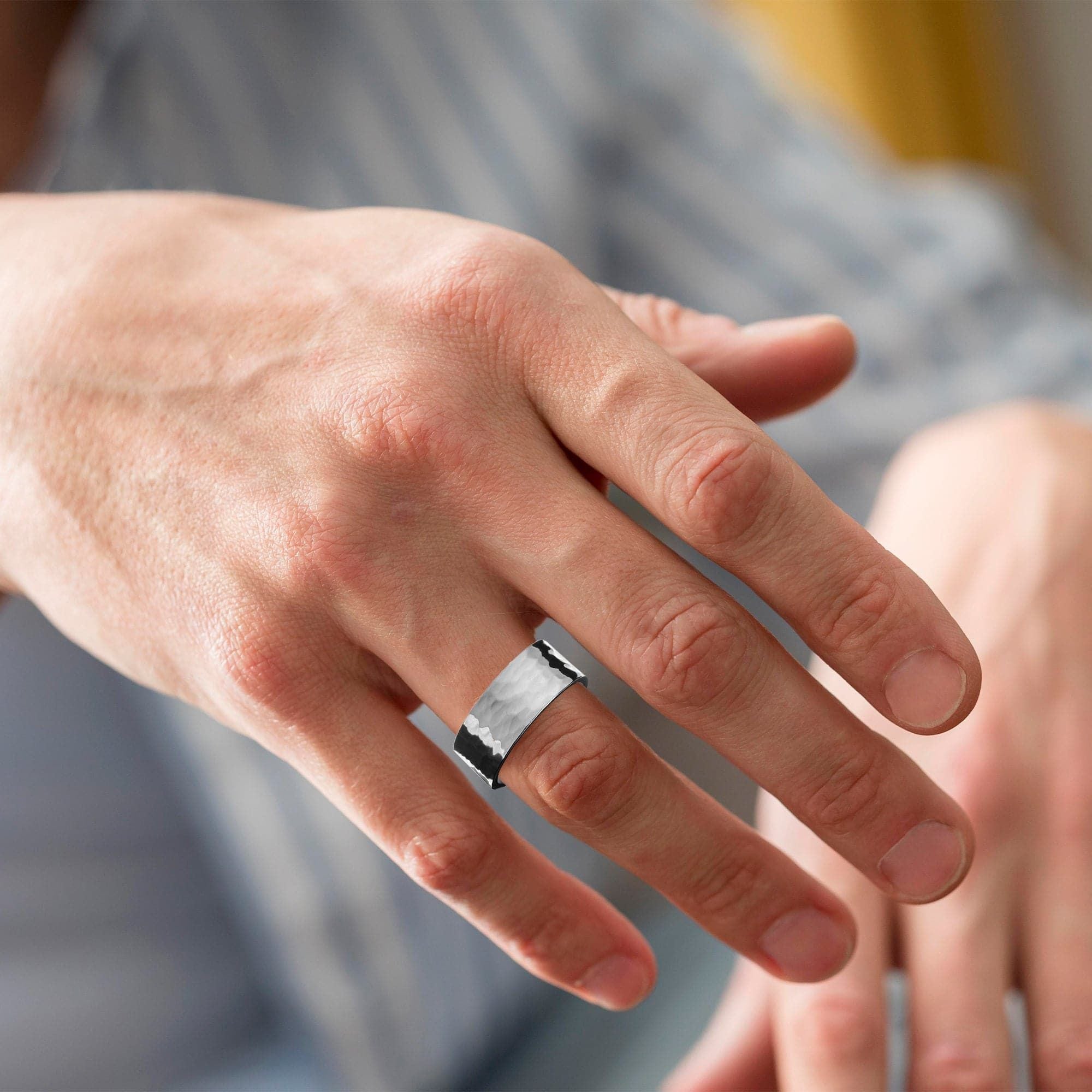 Silver ring on a finger showcasing a Men’s 9.5mm Hammered Ring in wide recycled brass