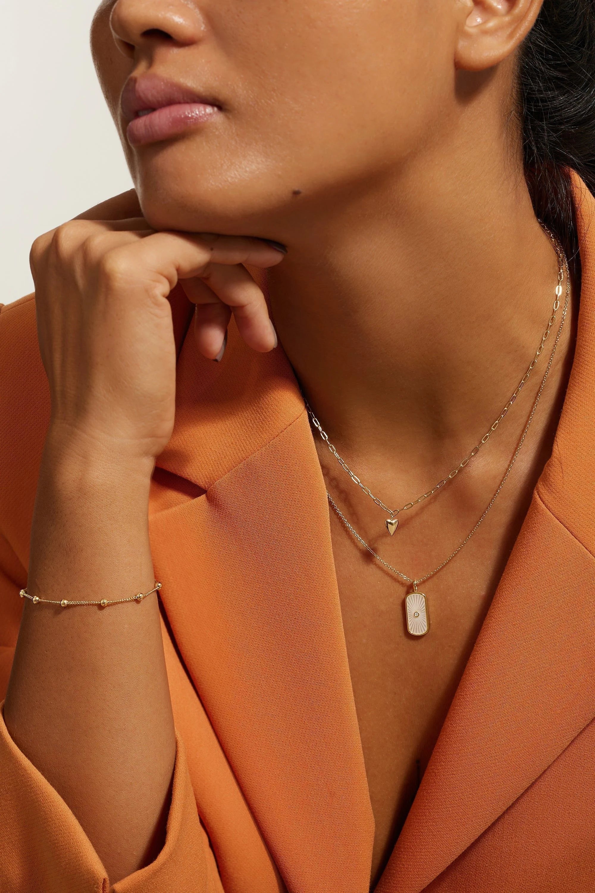 Woman wearing bright orange blazer and gold layered necklace with a paperclip design