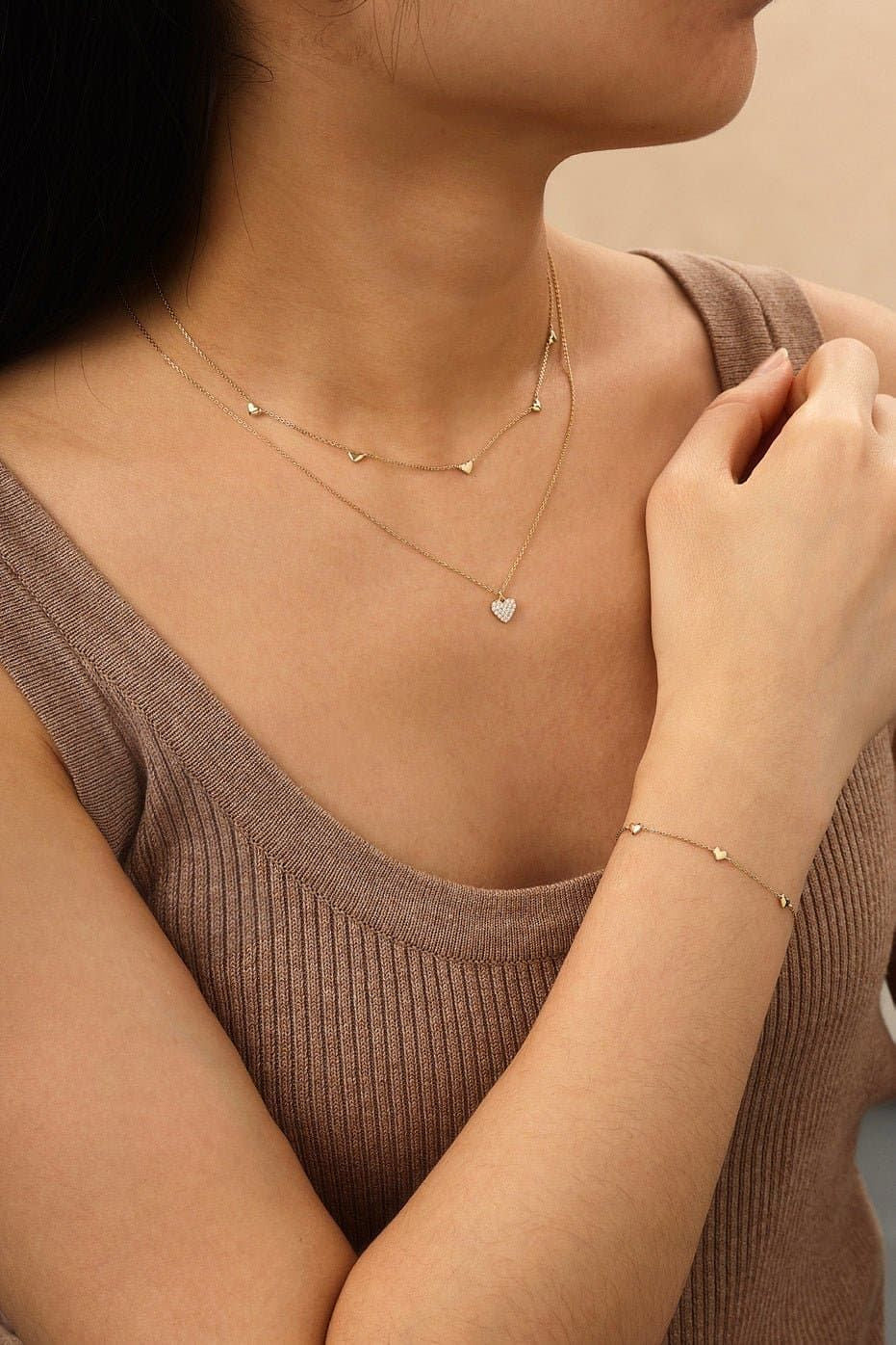 Woman showcasing a Multi Micro Heart Bracelet in 14k gold with matching necklaces