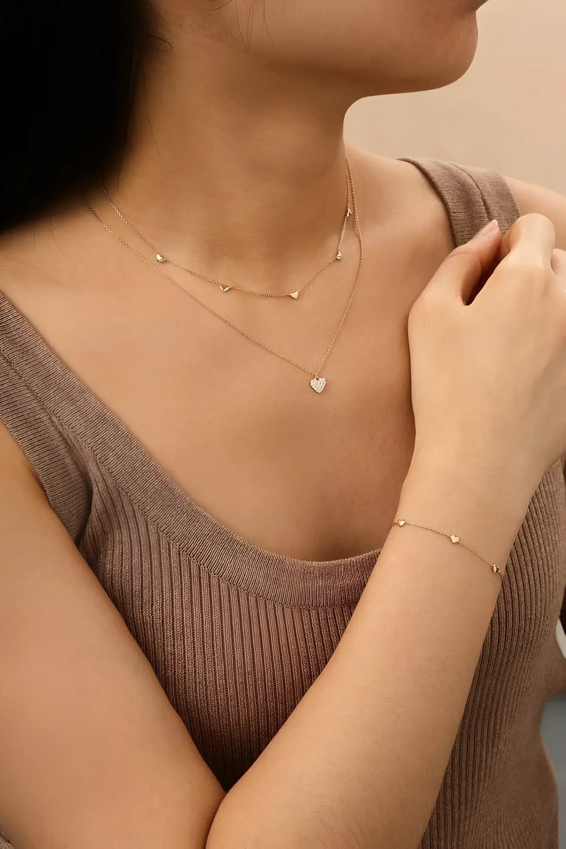 Woman showing off gold necklaces and bracelet from Multi Micro Heart Bracelet collection