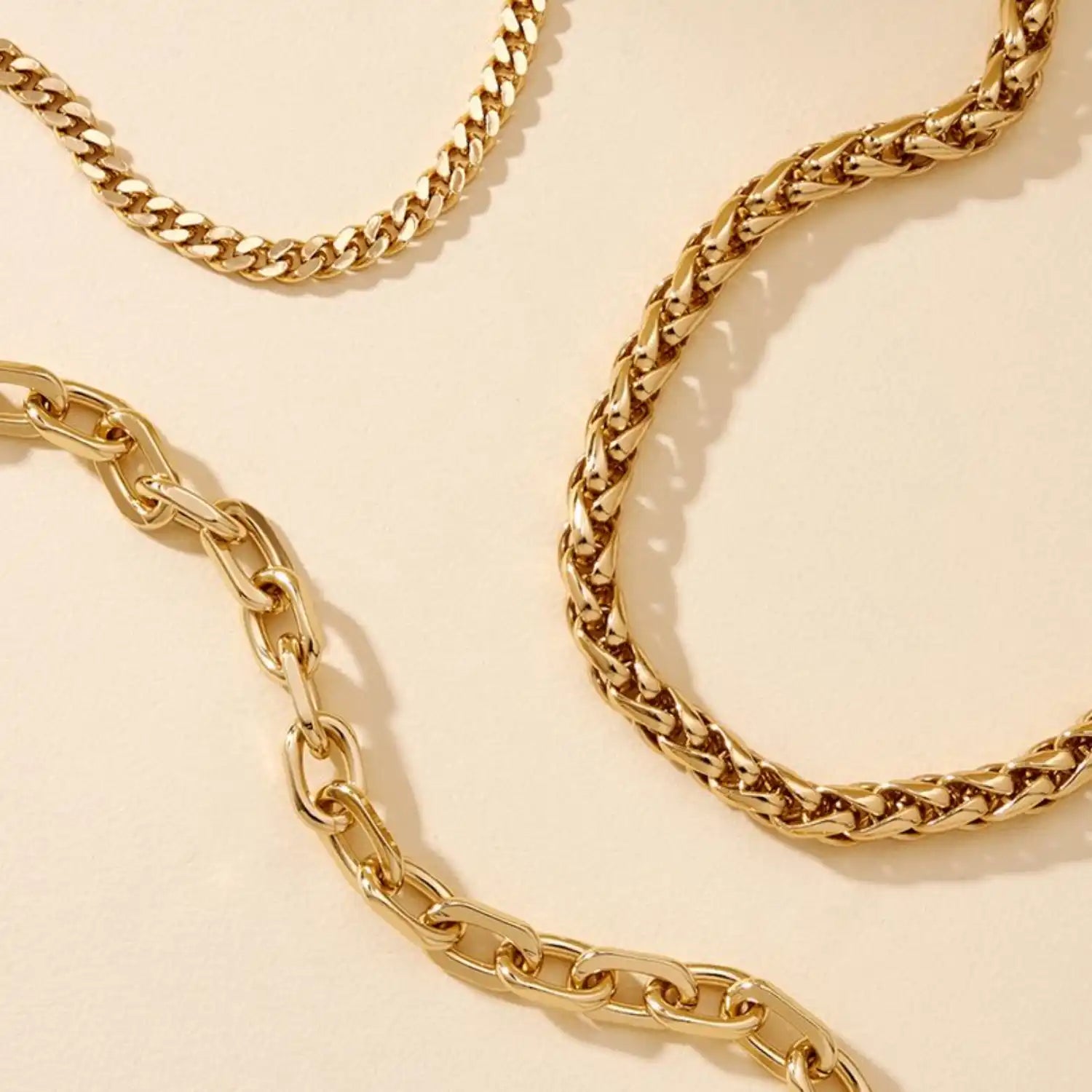 A set of three gold-colored chain necklaces, each with a distinct link pattern.