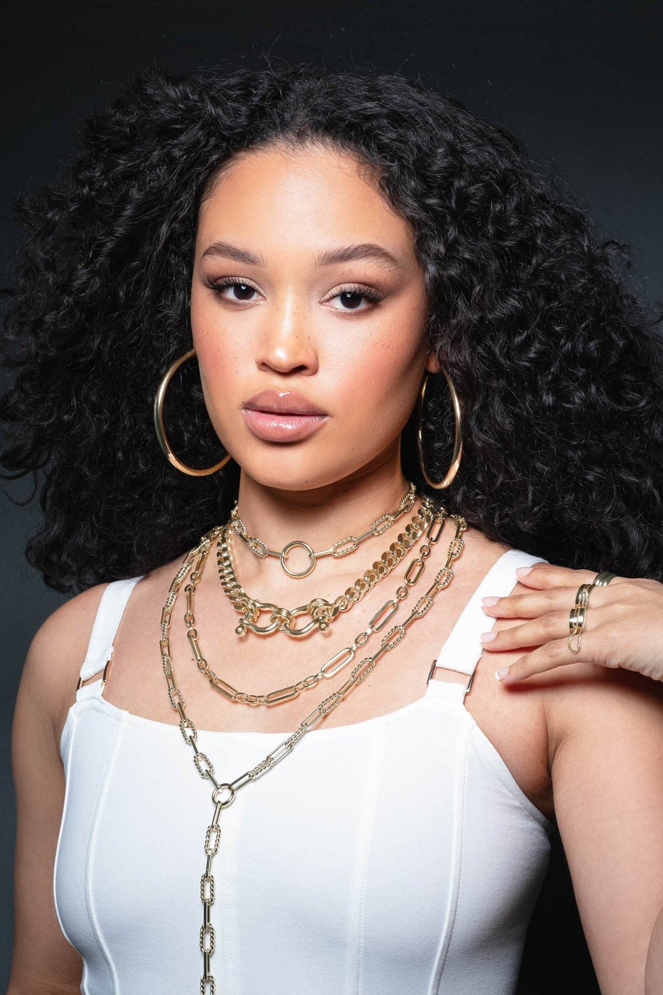 Woman showcasing the Skye Necklace with layered gold jewelry and a Cuban link chain