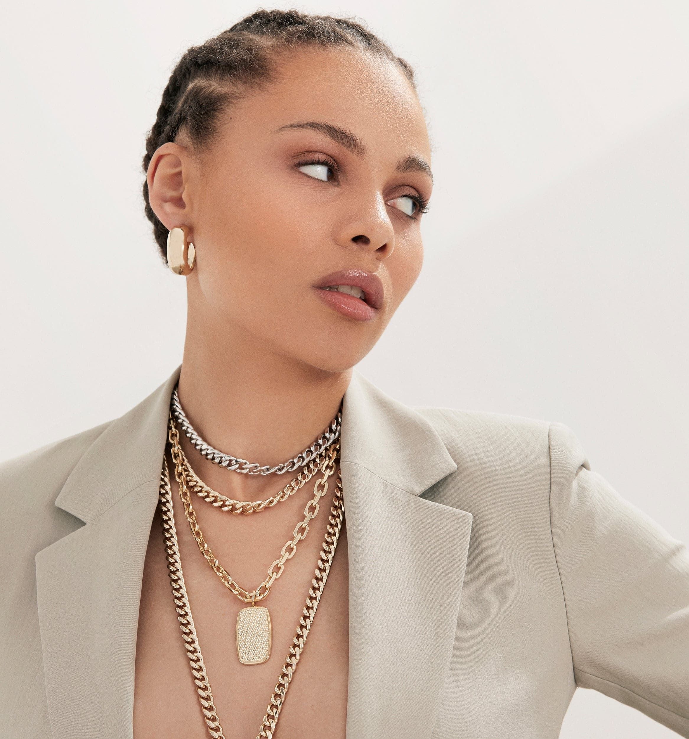 Woman showcasing the Valentina Necklace with layered gold necklaces and rounded Cuban link