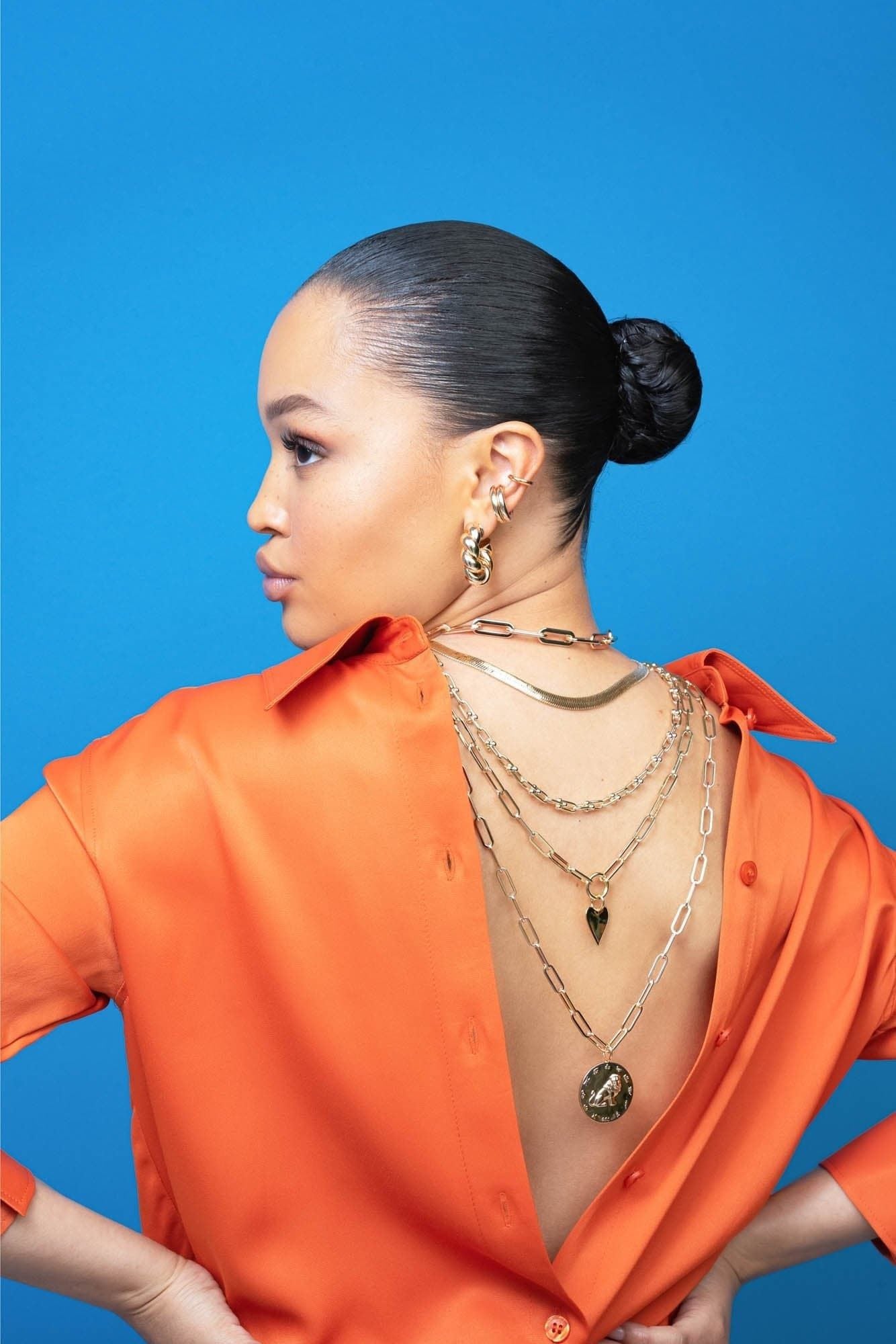 Woman in an orange shirt showcases the Zodiac Pendant Gemini and gold necklaces